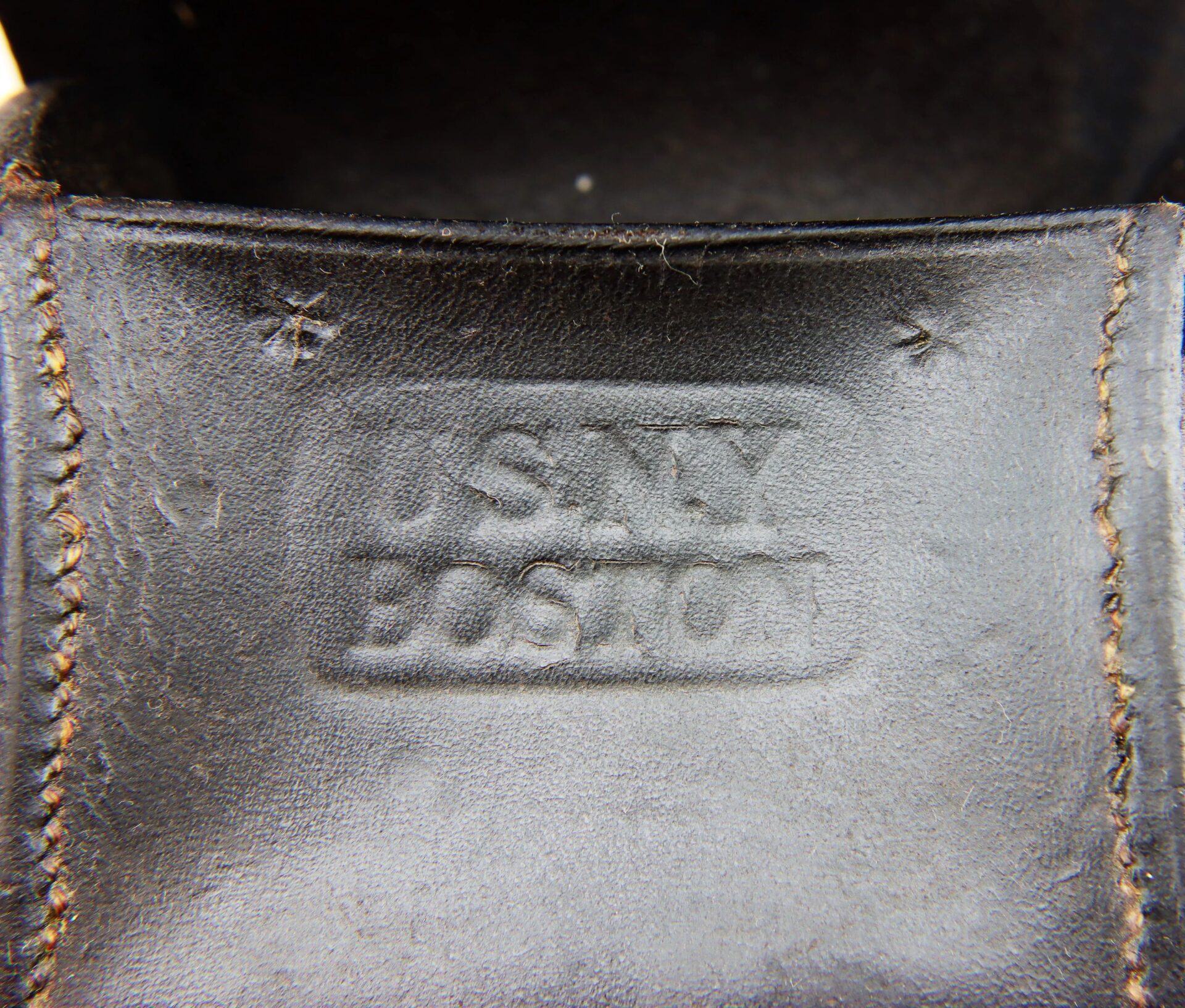 Close-up of the Civil War Navy Fuse Box, showing black leather with partially visible embossed text "U.S. NAVY BOSTON" between two stitched seams.