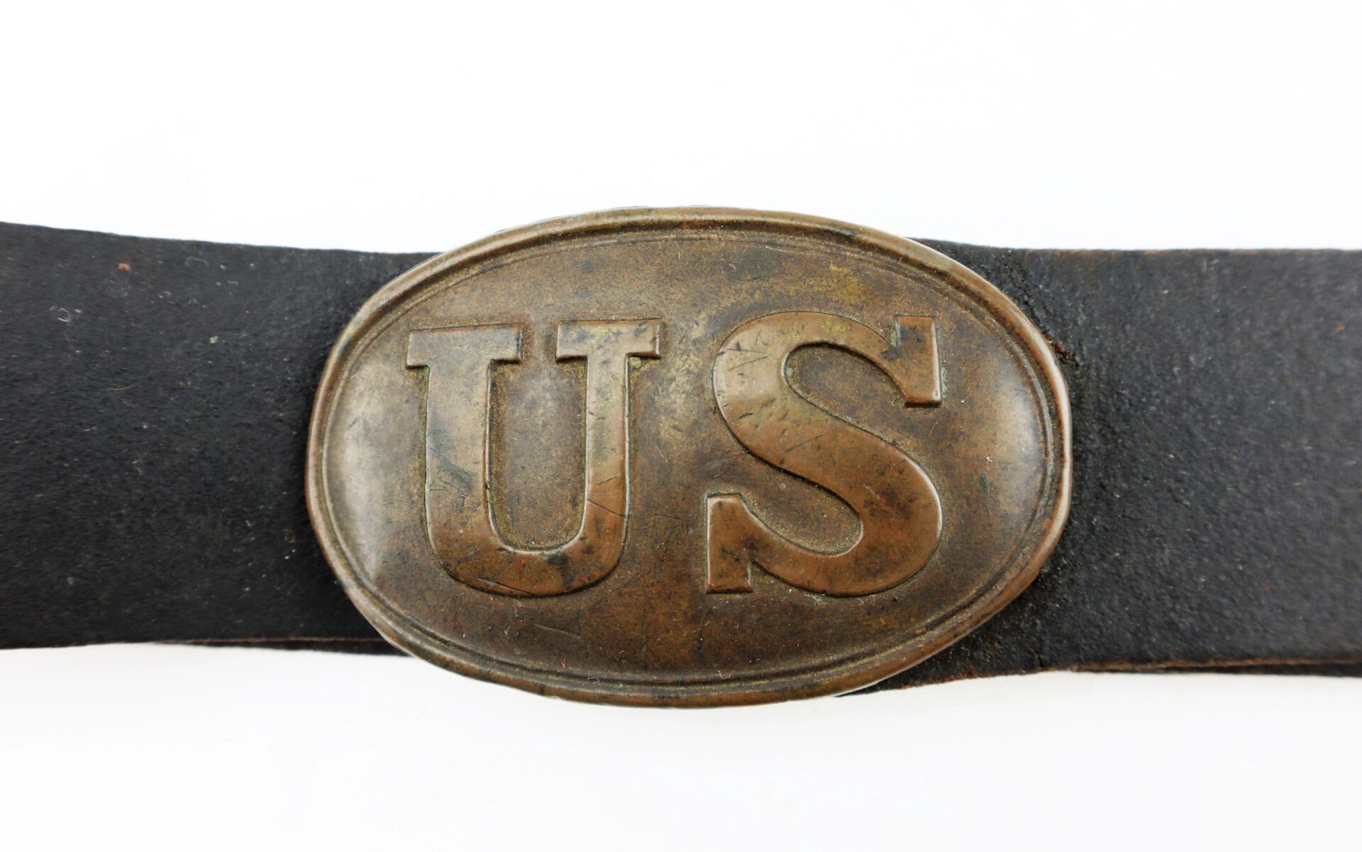A close-up of the U.S. Enlistedman’s Belt, marked “A.B. Covell,” shows a worn metal buckle with raised "US" letters on a dark leather strap.
