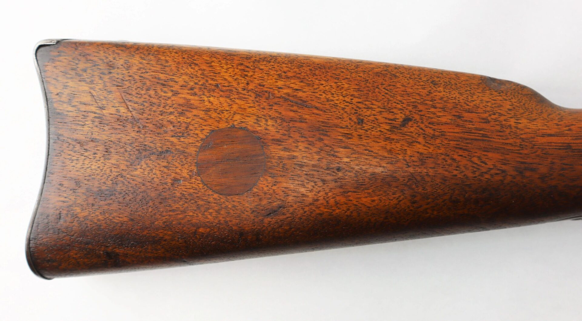 Close-up of the Confederate “Captured and Collected” Model 1861 Springfield Rifle-Musket wooden stock, featuring a round dark patch in the center and a metal buttplate at the end.
