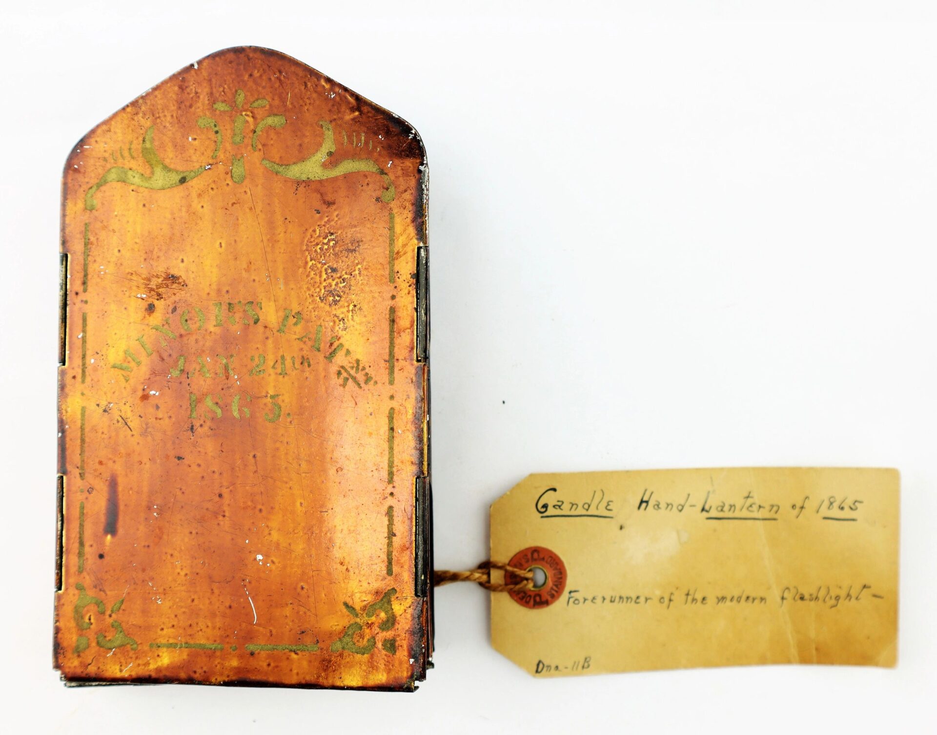 A Civil War Era Minor’s Patent Lantern from 1865, featuring a metal body with brown finish, green decorative accents, and an attached label calling it a forerunner of the modern flashlight.