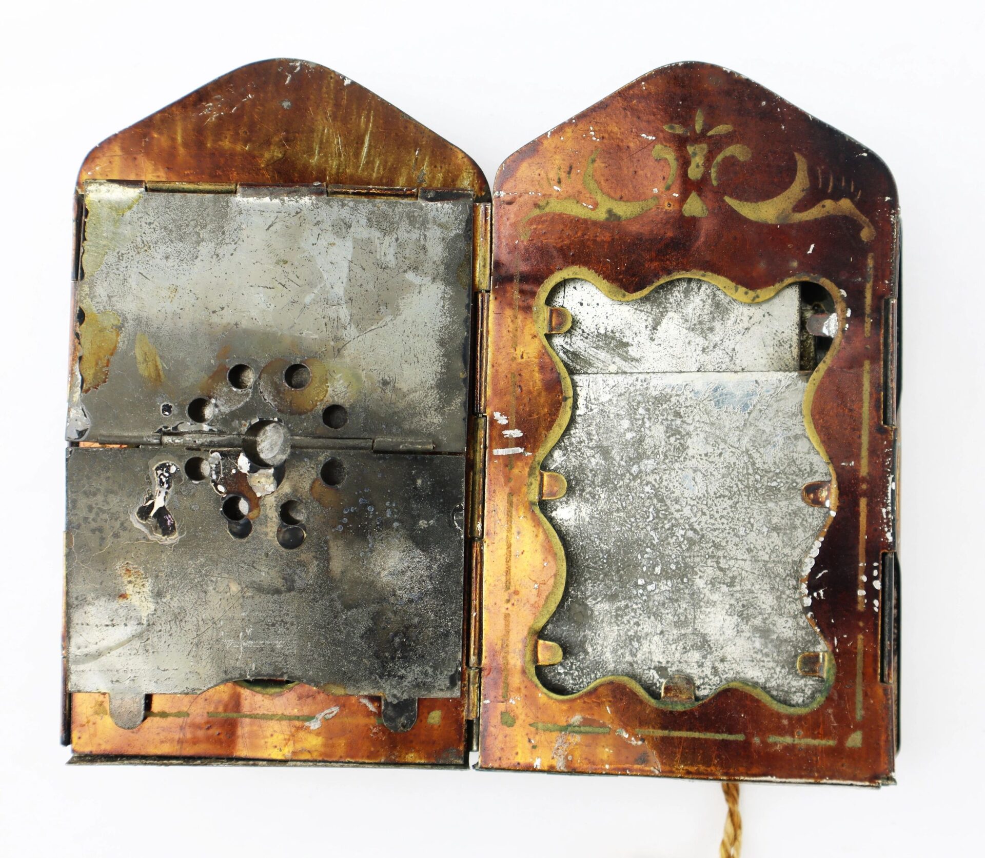 An opened, tarnished Civil War Era Minor’s Patent Lantern case features decorative edges; one side has multiple round perforations, while the other displays a shaped border framing a reflective surface.