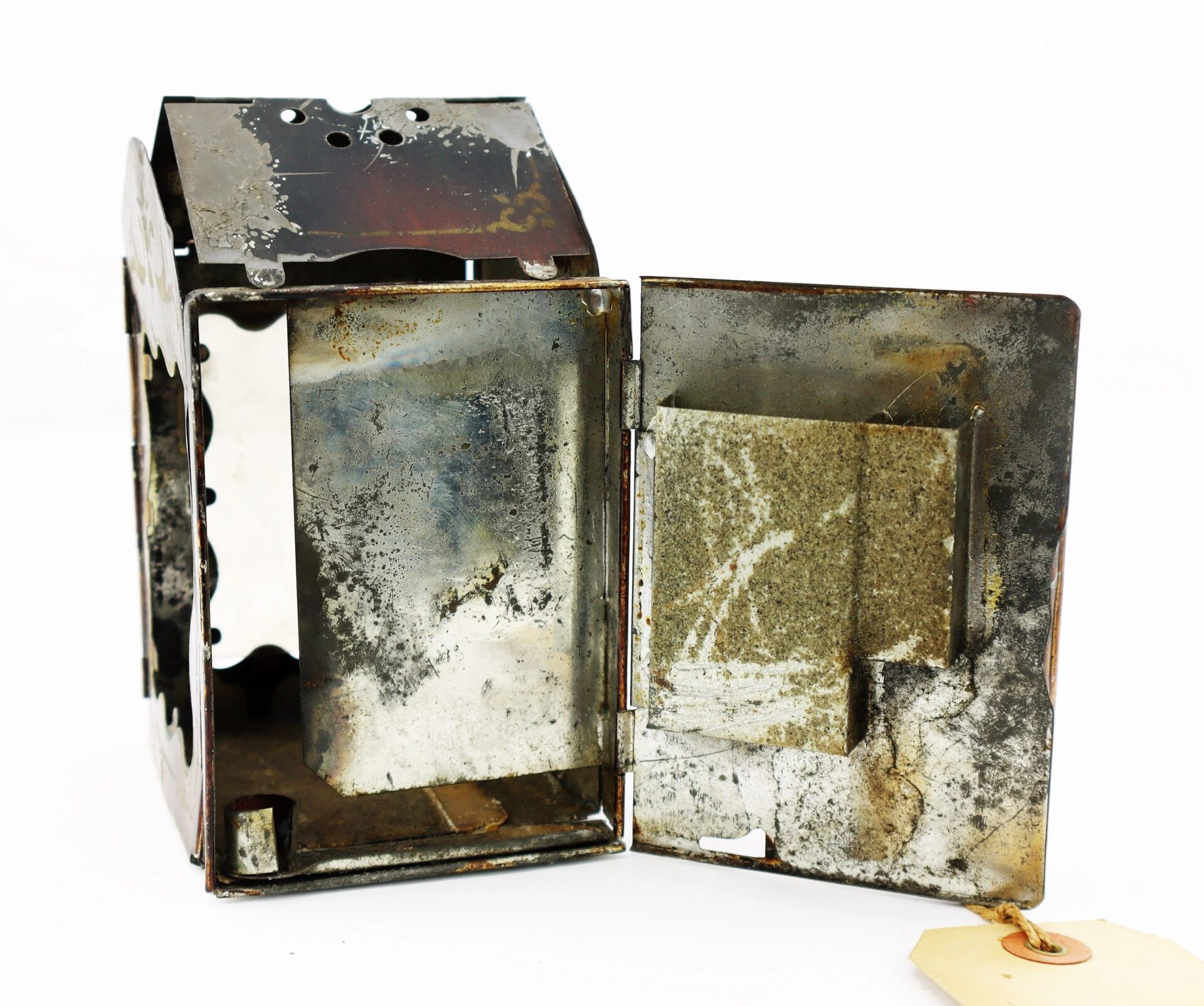 The Civil War Era Minor’s Patent Lantern is a rusted, rectangular metal box with an open front door, revealing a corroded interior and thick slab inside; a small tag hangs from the door.