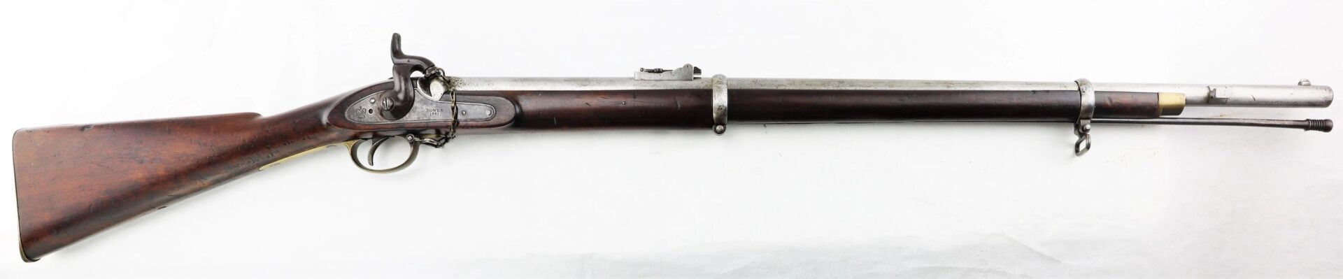 Side view of a Commercial Enfield Rifle, featuring a wooden stock, metal barrel, and ramrod, displayed on a white background.