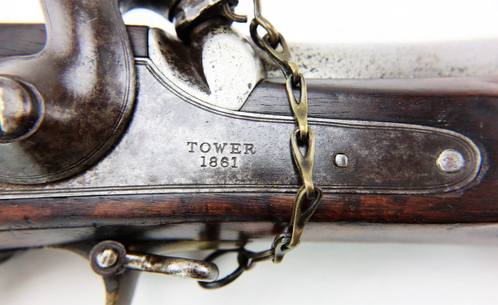 Close-up of a metal plate on a Commercial Enfield Rifle engraved with "TOWER 1861," showing part of a chain draped over the firearm.