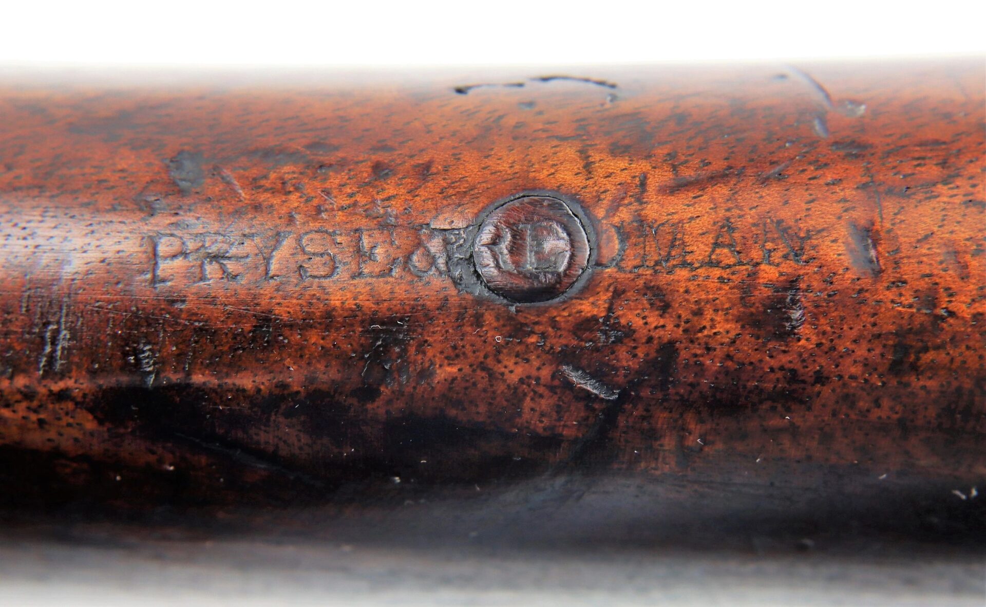 Close-up of a wooden Commercial Enfield Rifle surface, engraved with "PRYSE PATENT" and a circular stamp, displaying visible wear and aging.