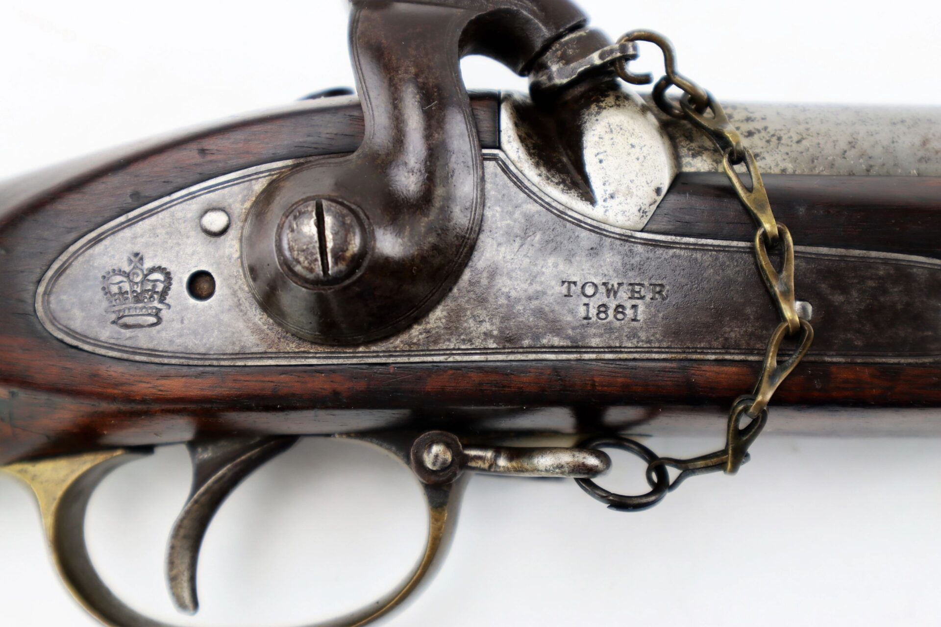 Close-up of a Commercial Enfield Rifle’s trigger and lock mechanism, engraved with “TOWER 1861” and a crown insignia, featuring an attached metal chain.