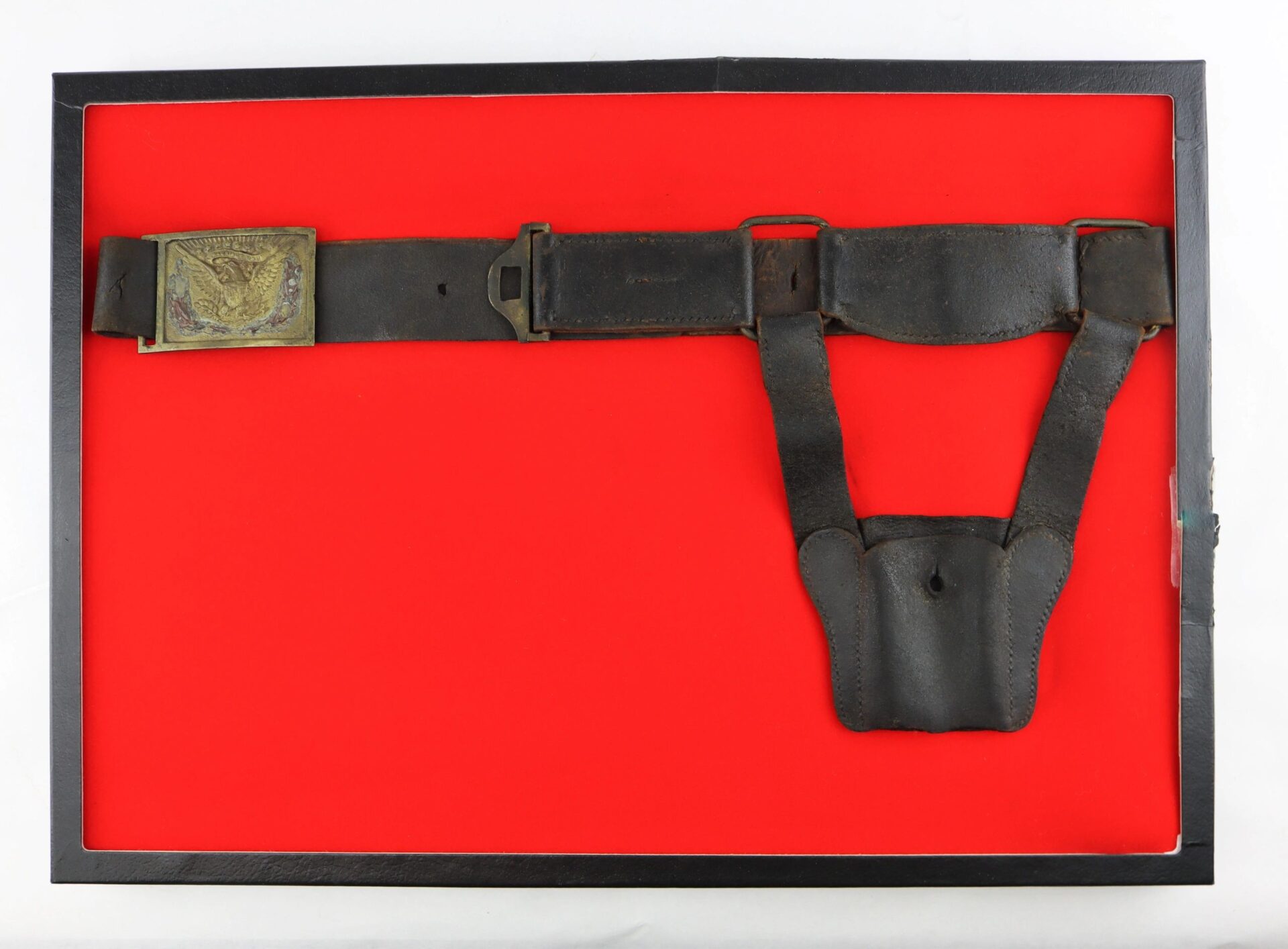 The U.S. Foot Artillery Belt is a vintage black leather military belt with a brass buckle and attached pouch, showcased in a black frame with a red background.