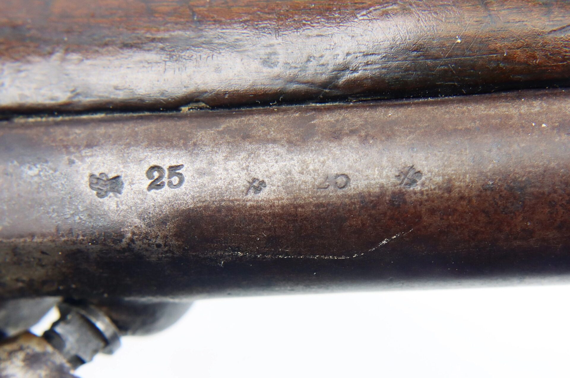 Close-up of a metal surface on the Confederate 1863 Dated Enfield Altered to a Cavalry Carbine, showing engraved markings with the numbers "25" and "20," symbols beside them, and a wooden part visible above.