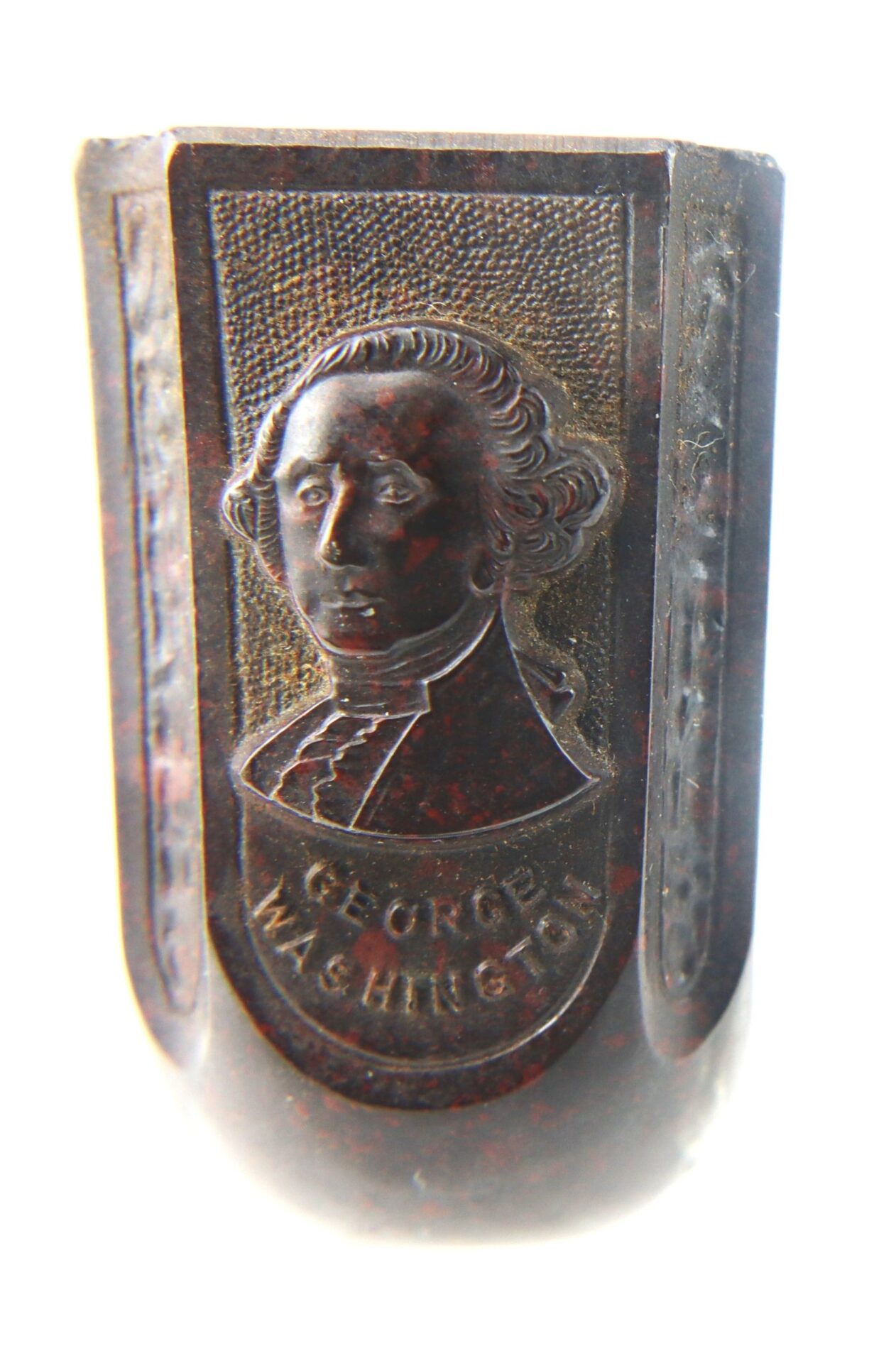 A close-up of the General George Washington Gutta-Percha Pipe (ca. 1850), a dark object displaying a raised portrait of George Washington with his name engraved beneath the image.