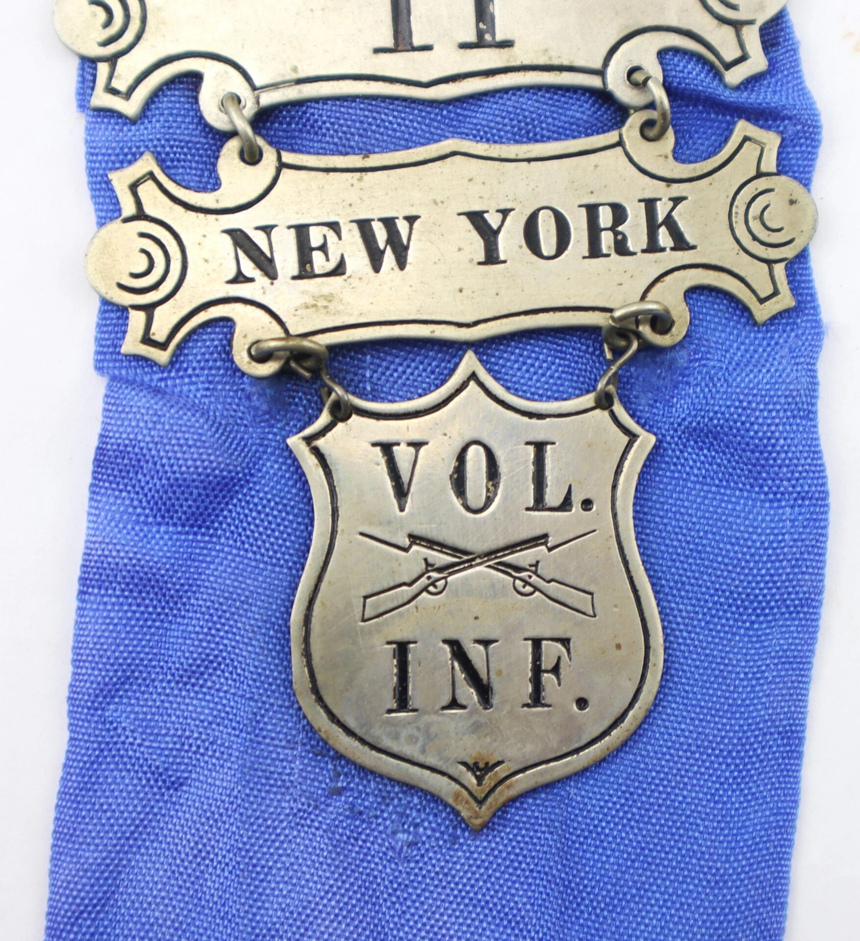 A Ladder Badge for the 11th New York Infantry “Ellsworth Zouaves,” marked SOLD, shown on a blue fabric background.