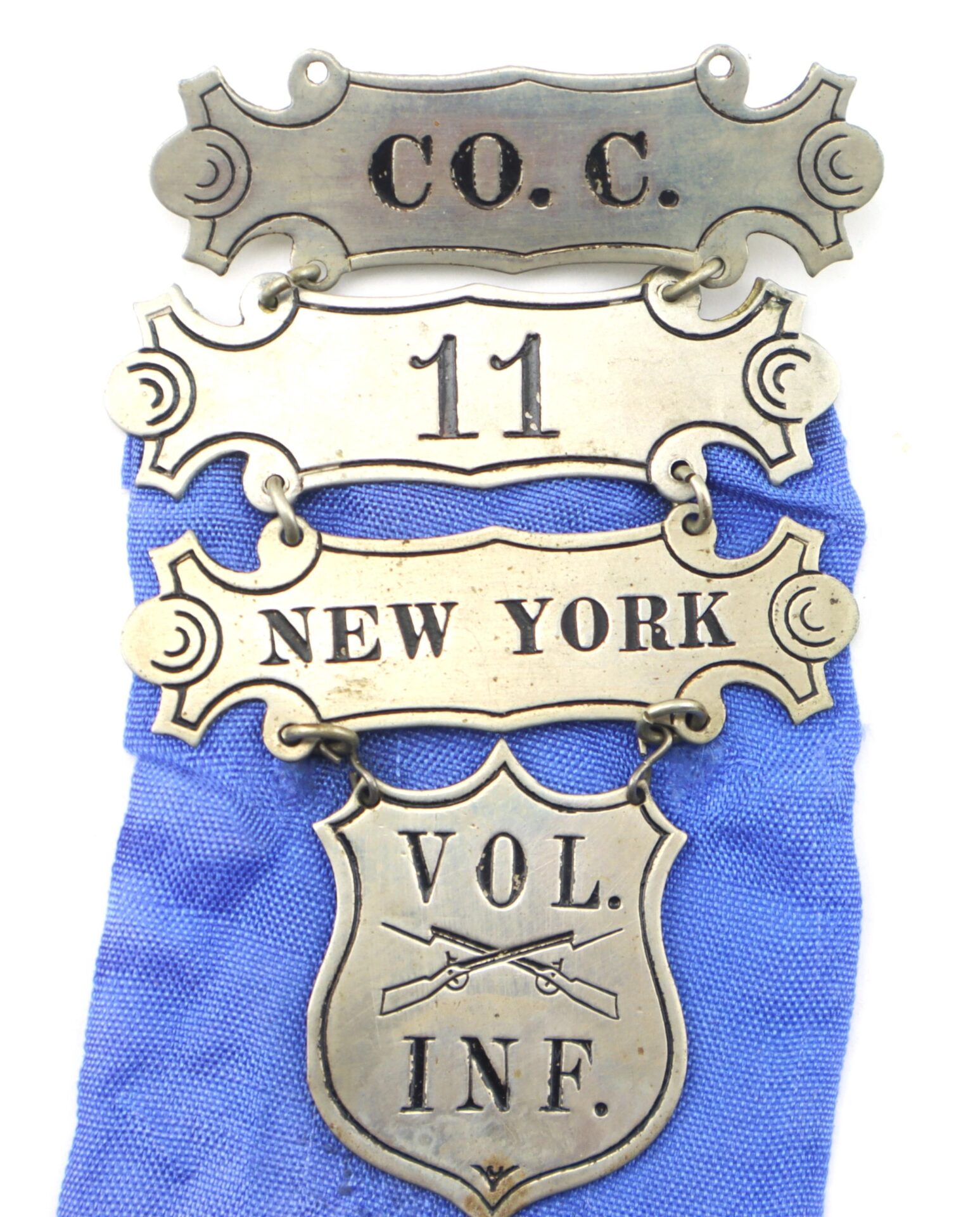 Ladder Badge for the 11th New York Infantry “Ellsworth Zouaves”—a metal badge in four sections: “C.O.C.,” “11,” “NEW YORK,” and a shield with “VOL. INF.” over blue cloth background. / SOLD.