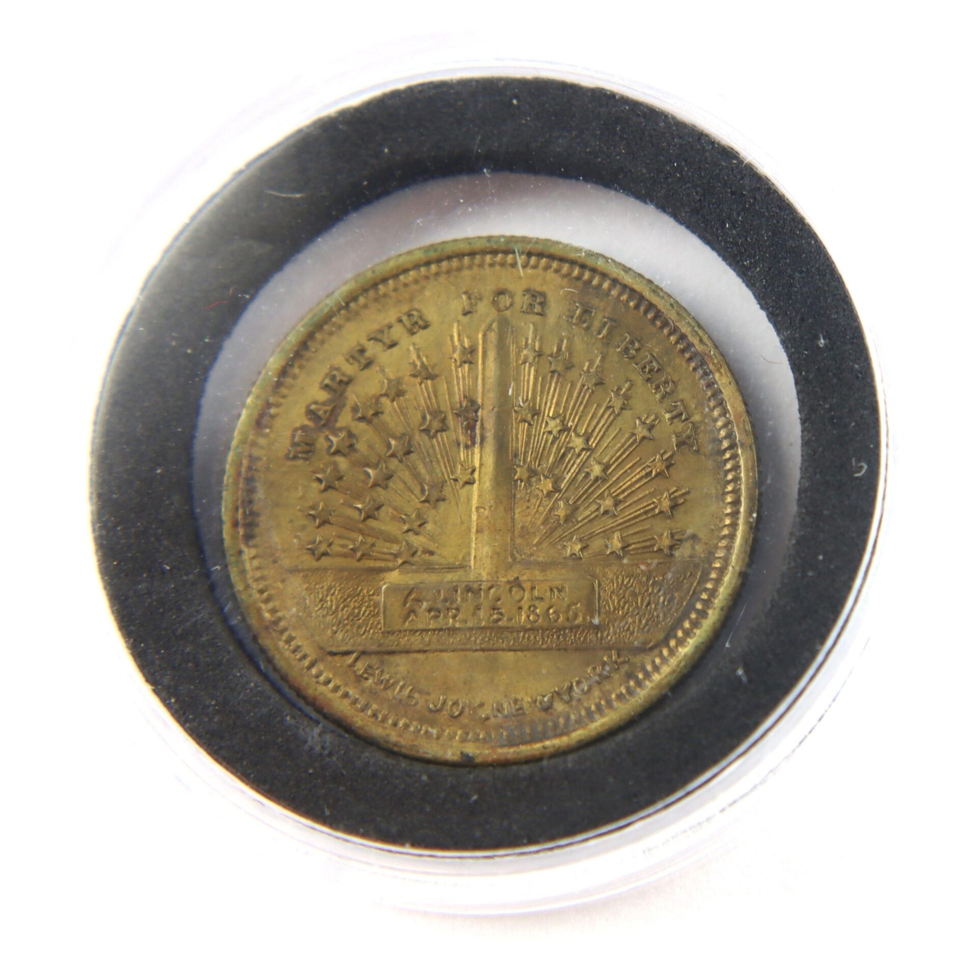 The Abraham Lincoln Assassination Token is a commemorative coin in a clear round case, featuring an obelisk, stars, and the inscription "EMANCIPATION APRIL 25 1865.