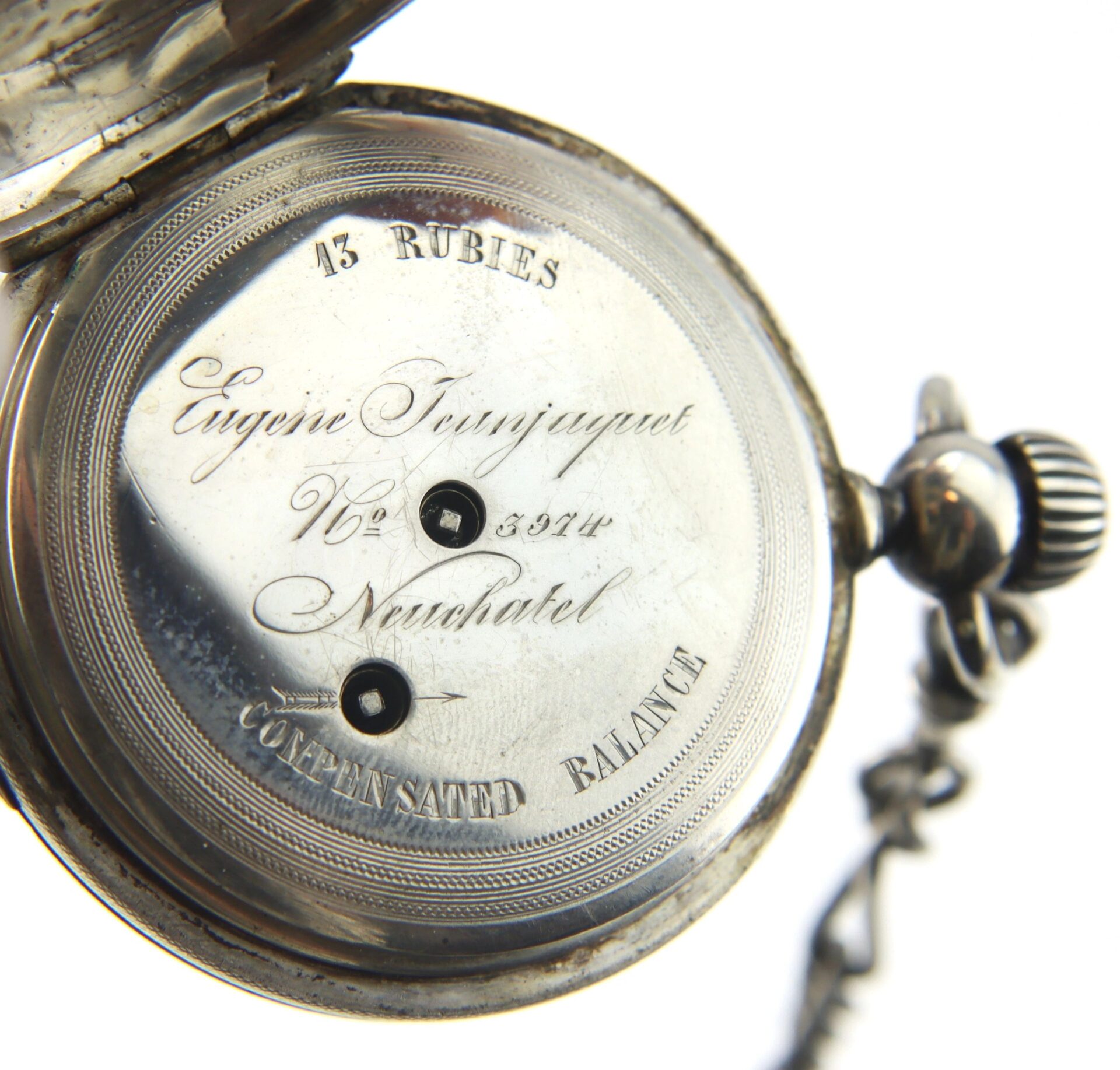 Close-up of an open Silver Presentation “Life Saving” Watch showing engraved text such as "13 Rubies," "Eugène Joujaquet," and "Neuchatel," with winding holes and a visible chain.