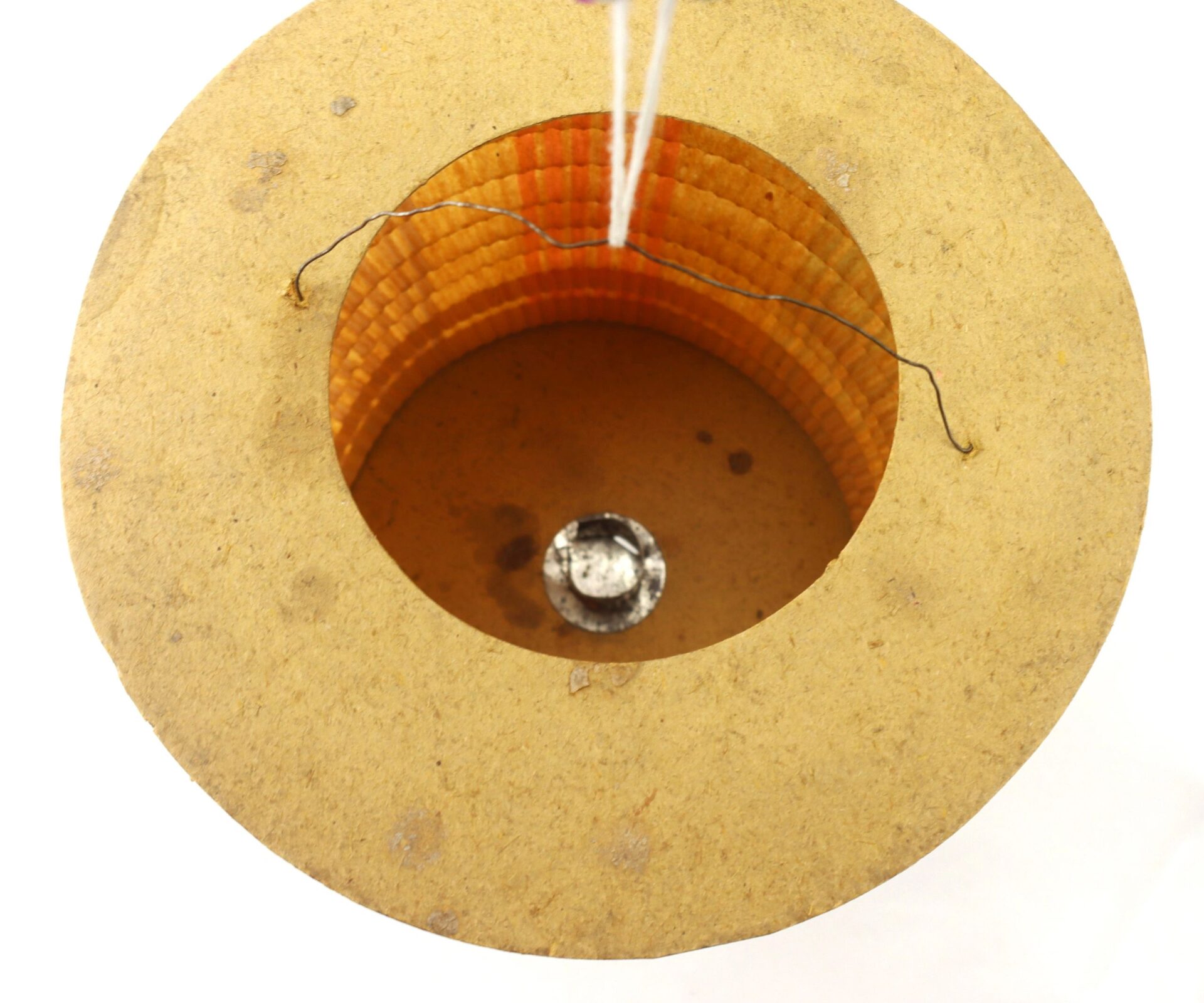 A top-down view of the Political Parade Lantern, featuring a cylindrical coil with wire and a round metallic component at the center, all set in a beige circular base.