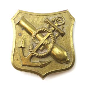 The Attractive 9th Corps Badge is a brass military badge featuring an anchor, rope, and cannon on a textured shield-shaped background.
