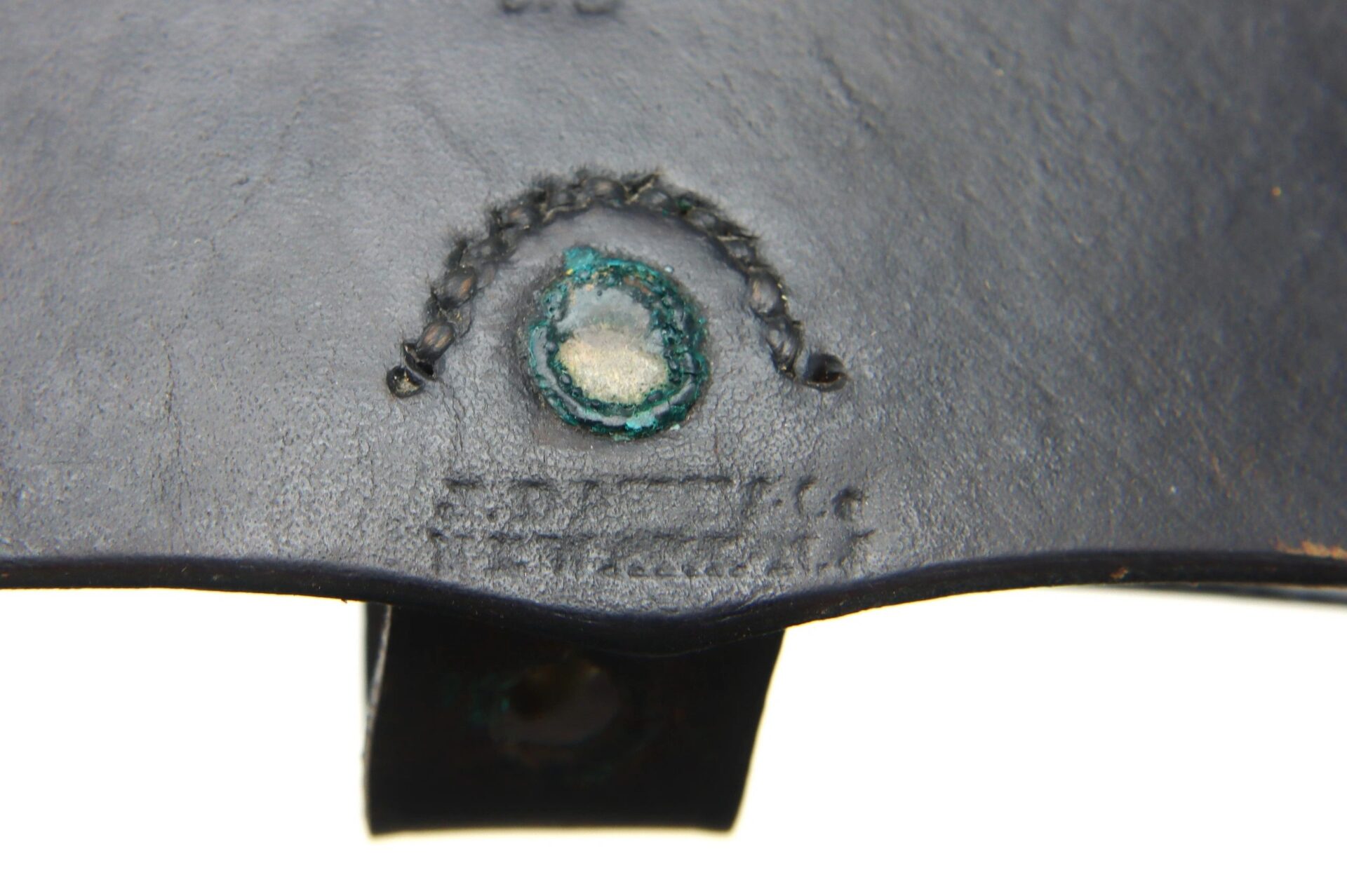 Close-up of the dark leather surface of a Pistol Cartridge Box (SOLD), featuring a greenish-blue circular stain, visible stitching, and an embossed stamp with faint, unreadable text.