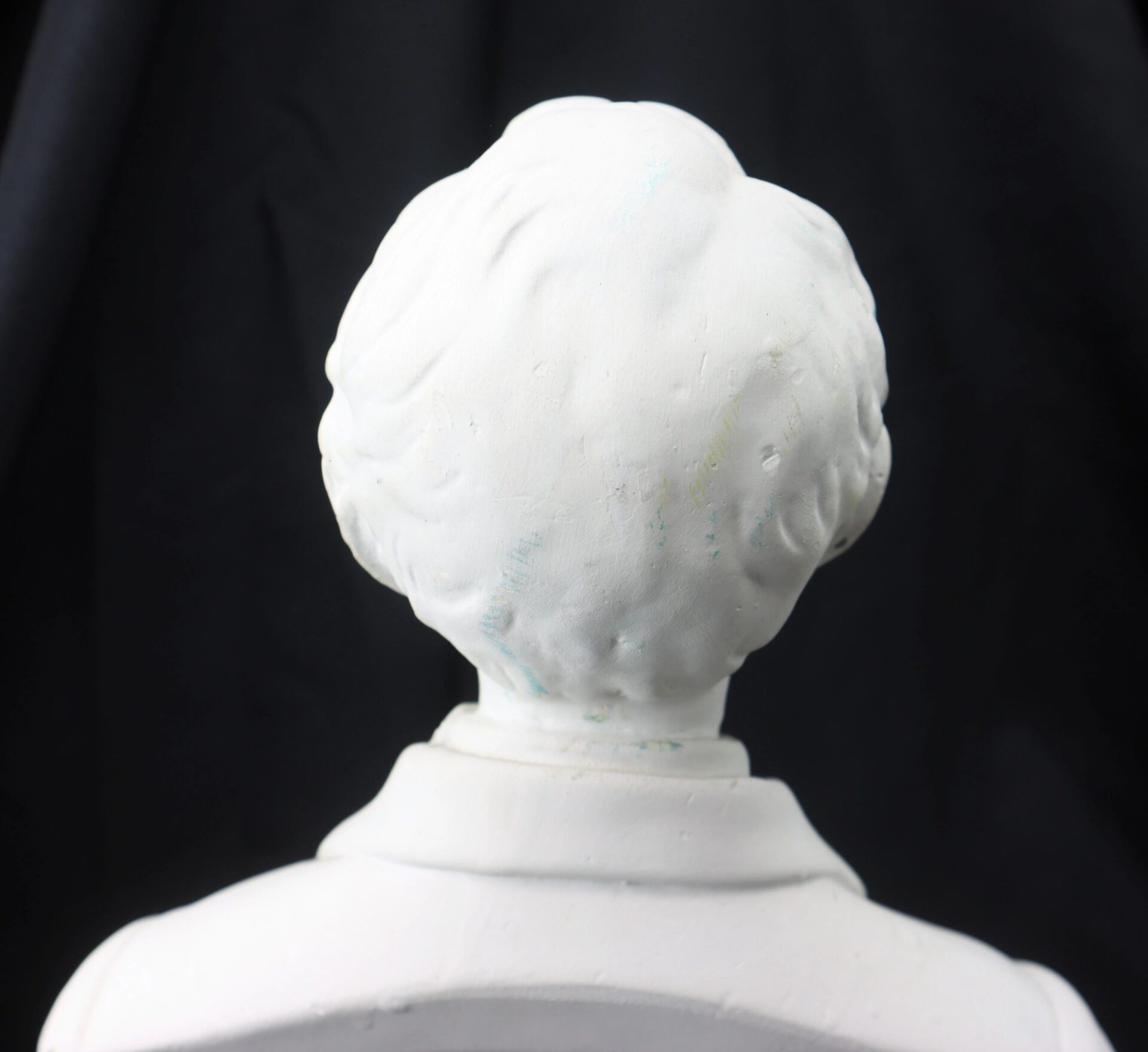 White bust sculpture of Abraham Lincoln viewed from behind, showing the back of his head and shoulders against a plain black background.
