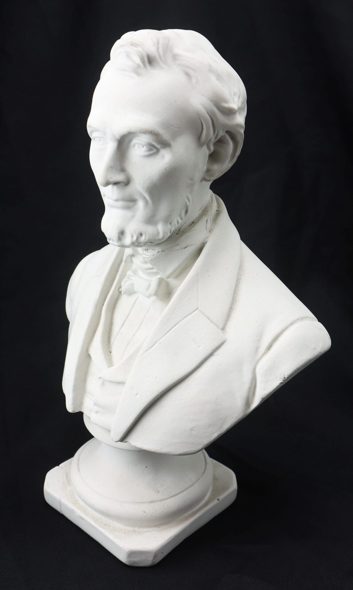 White plaster bust of Abraham Lincoln in a suit, displayed against a plain black background.