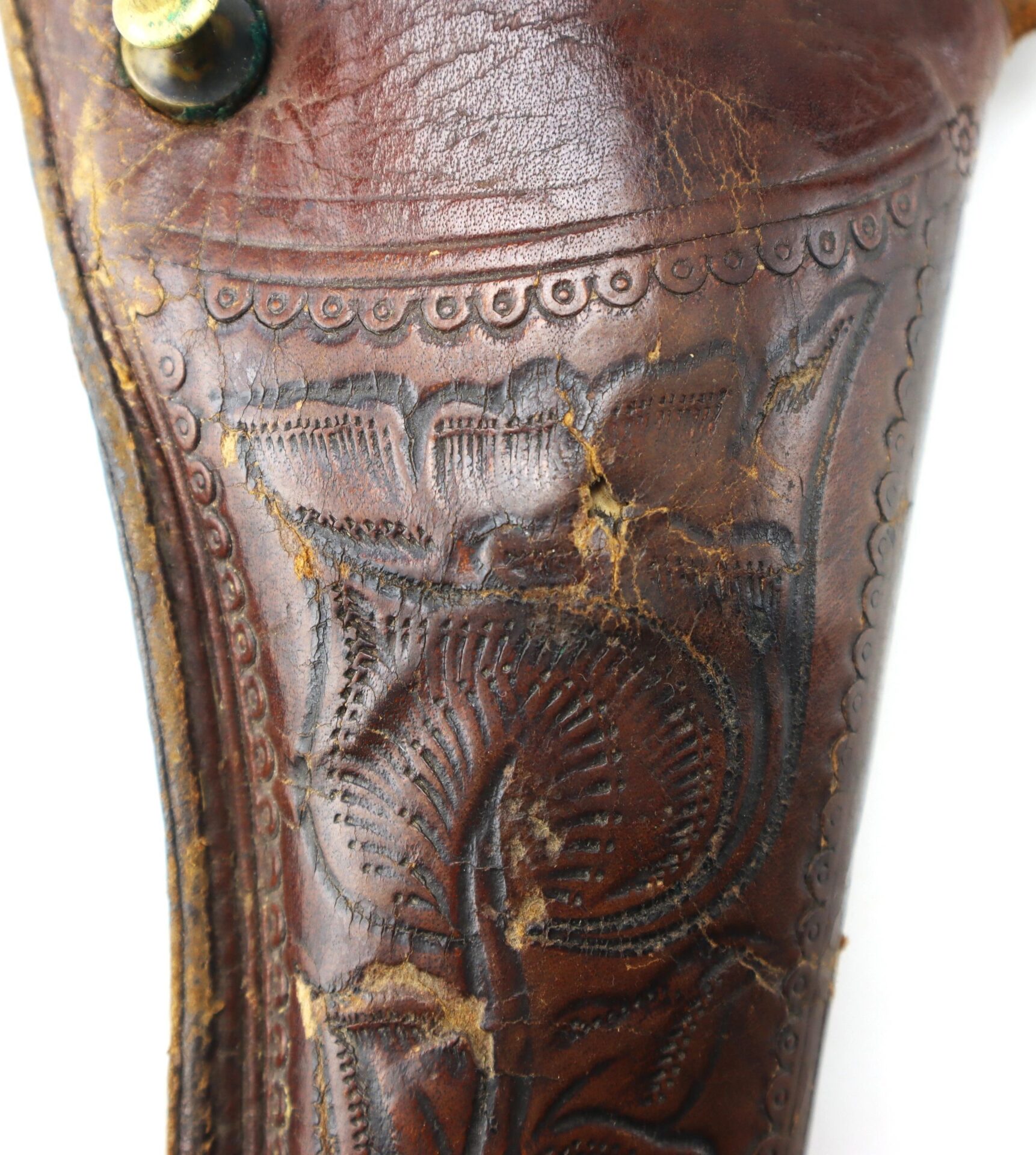 Close-up of the Wonderful “Rose of Texas” Holster, a worn brown leather piece featuring detailed floral tooling and visible surface cracks.