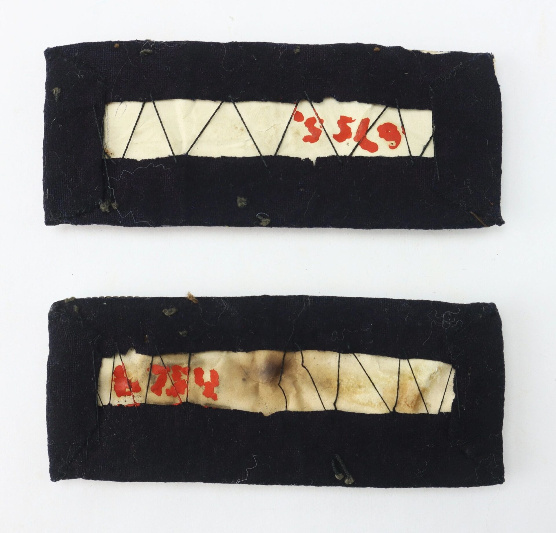 A pair of Colonel of Staff Shoulder Bars: rectangular black fabric patches with white centers, featuring red handwritten numbers and black stitched patterns on a white background.