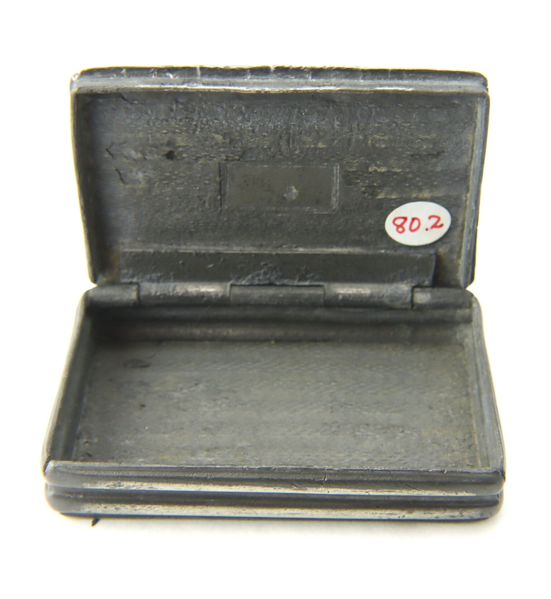 A small, rectangular hinged metal Civil War snuff box, open and empty inside, features a white sticker labeled "80.2" on the lid.