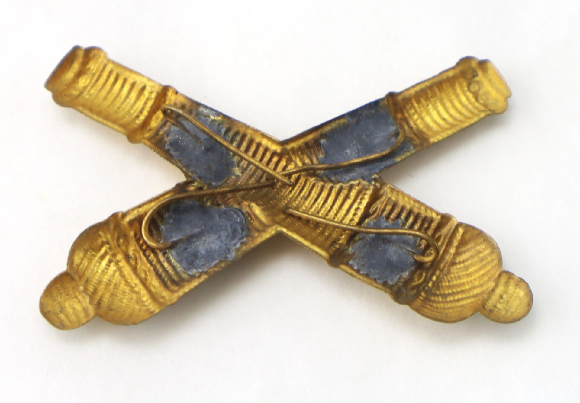 A Small Officer’s False Embroidered Cross Cannon brass insignia featuring two crossed cannons with visible wear and patina.