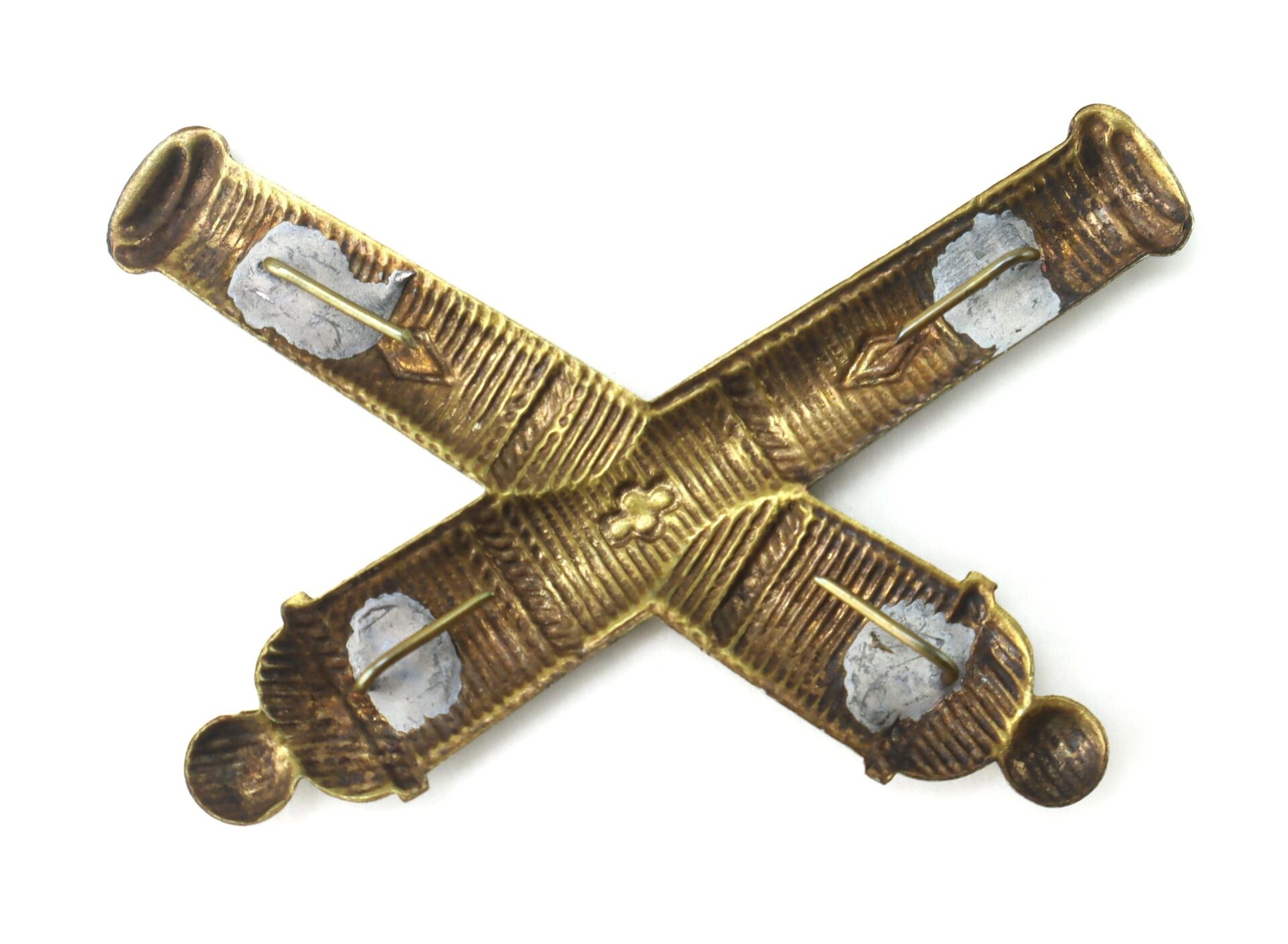 Officer’s False Embroidered Artillery Insignia, SOLD: Bronze crossed cannons with four end caps, a central floral emblem, engraved details, and visible wear.