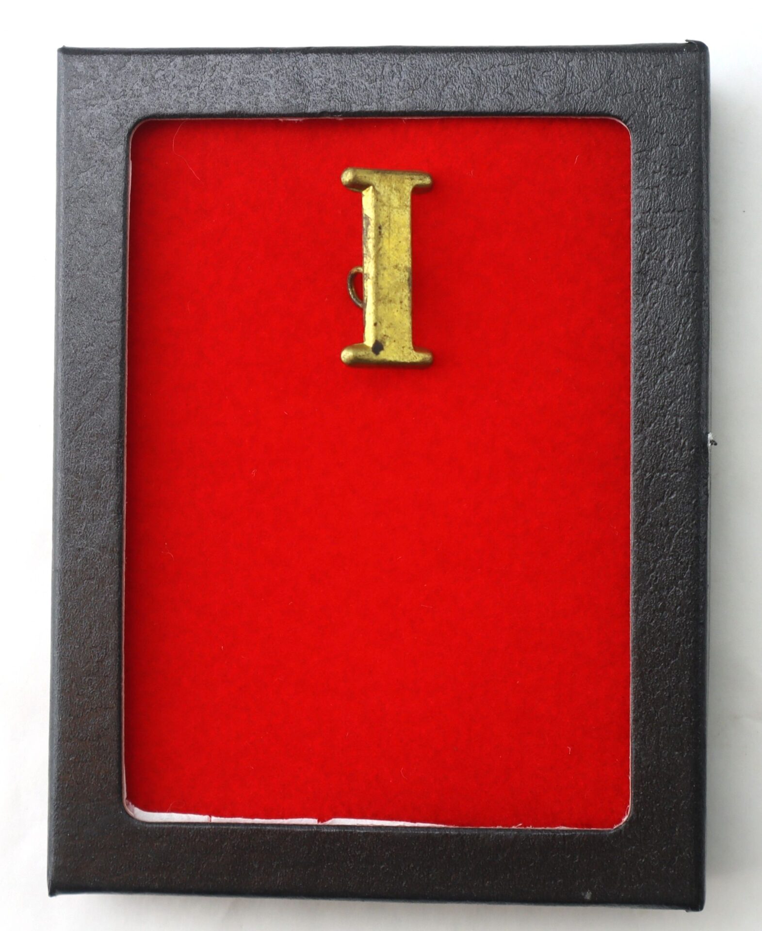 The Regimental Company Letter I gold pin is showcased at the center of a red felt background within a sleek black rectangular frame.