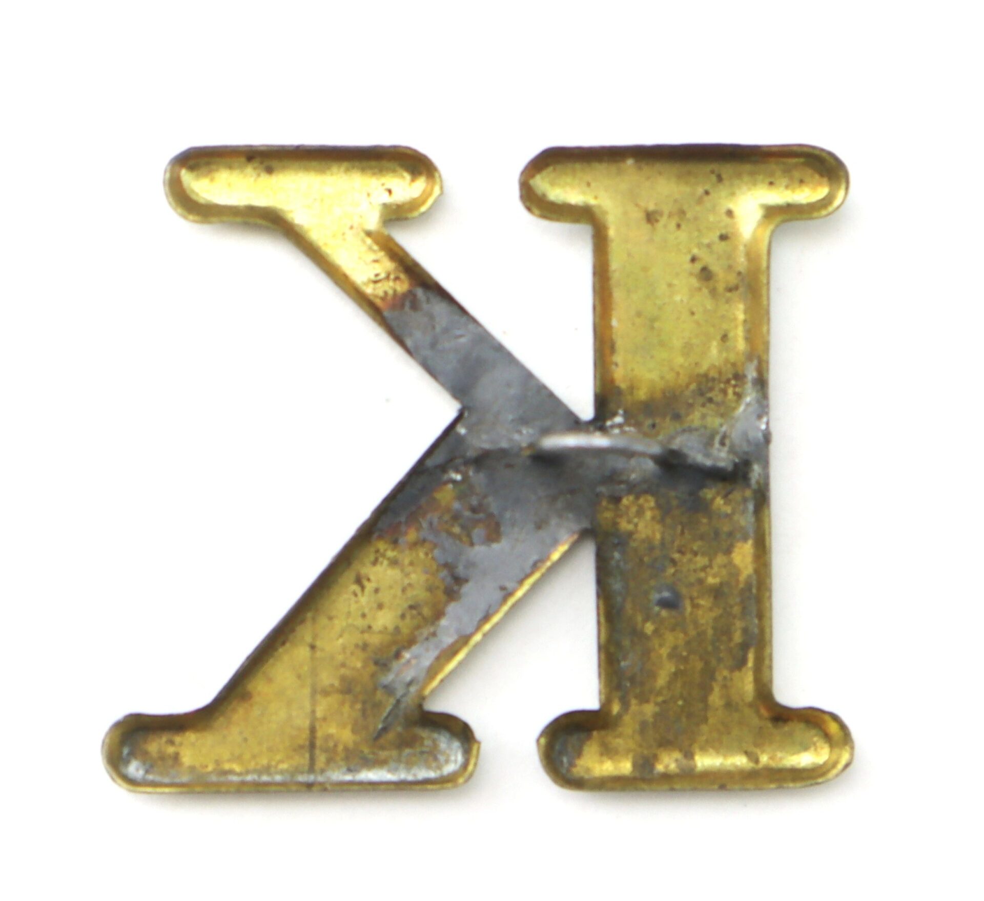 The Original Civil War Brass Hat Letter “K” Company Designation features a gold-toned finish with visible scratches, tarnish, and discoloration, showing authentic signs of age and wear.