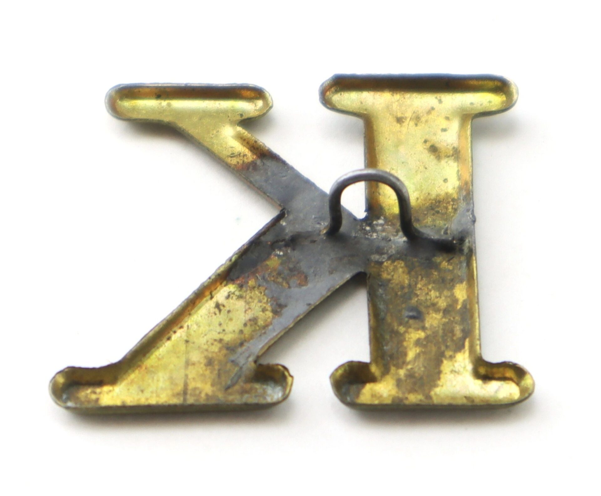 An Original Civil War Brass Hat Letter “K” Company Designation with visible solder marks and a metal hook on the back, shown on a white background.