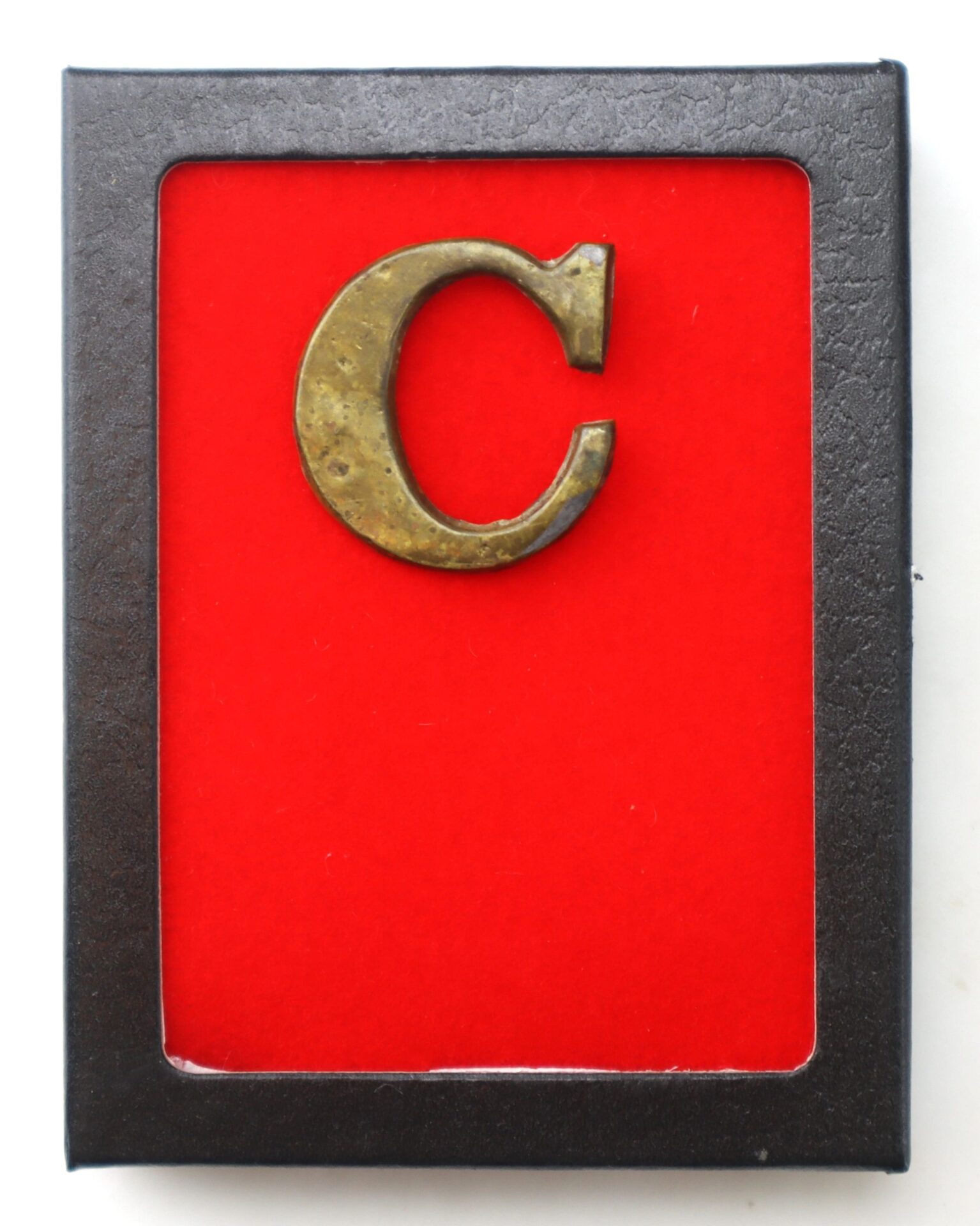 An Original Civil War Brass Hat Letter "C" – Company Designation, showcased on a red background within a black frame.
