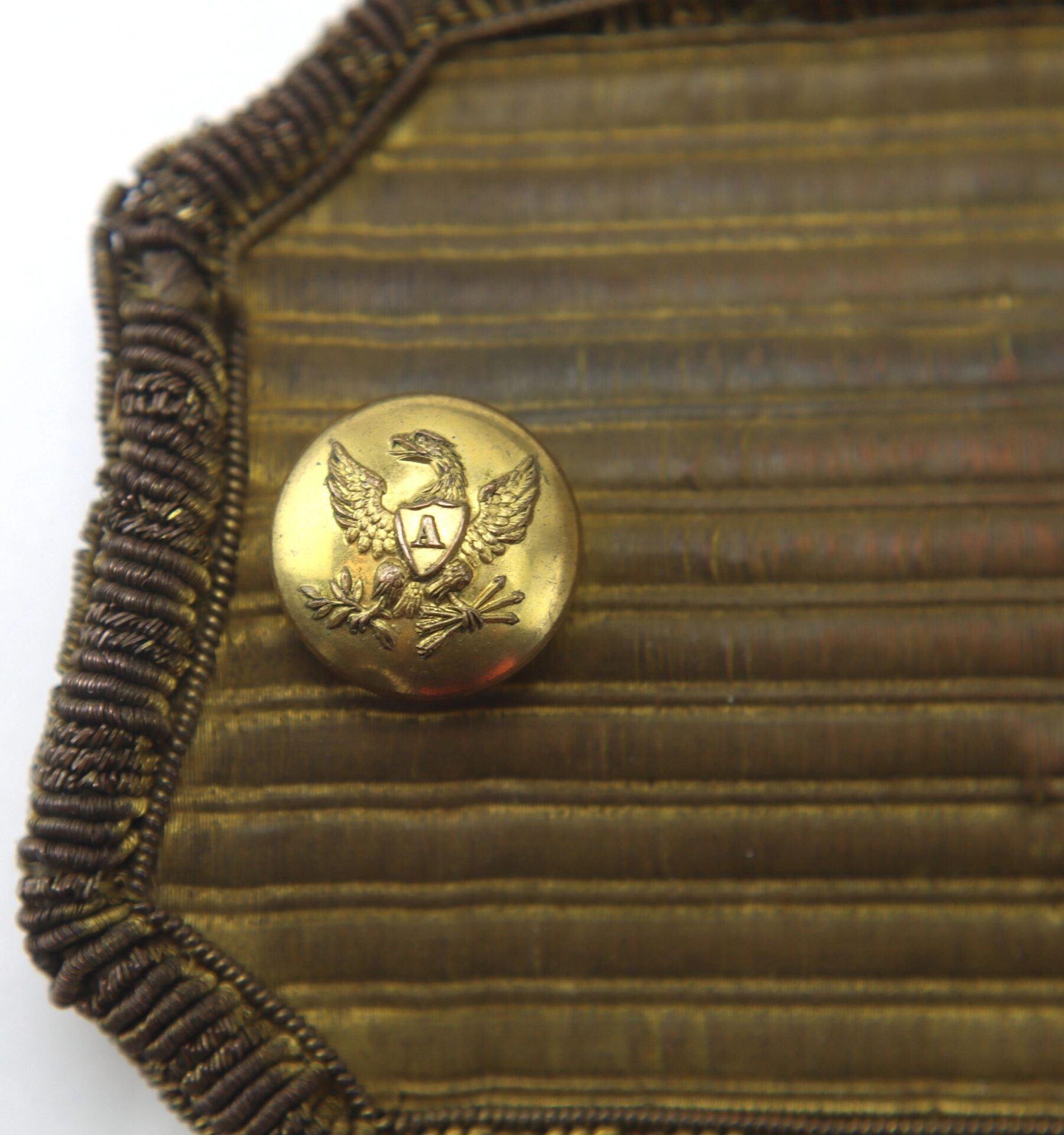 A gold eagle-emblem button sits on textured, gold-braided fabric from U.S. Officer’s Epaulettes.