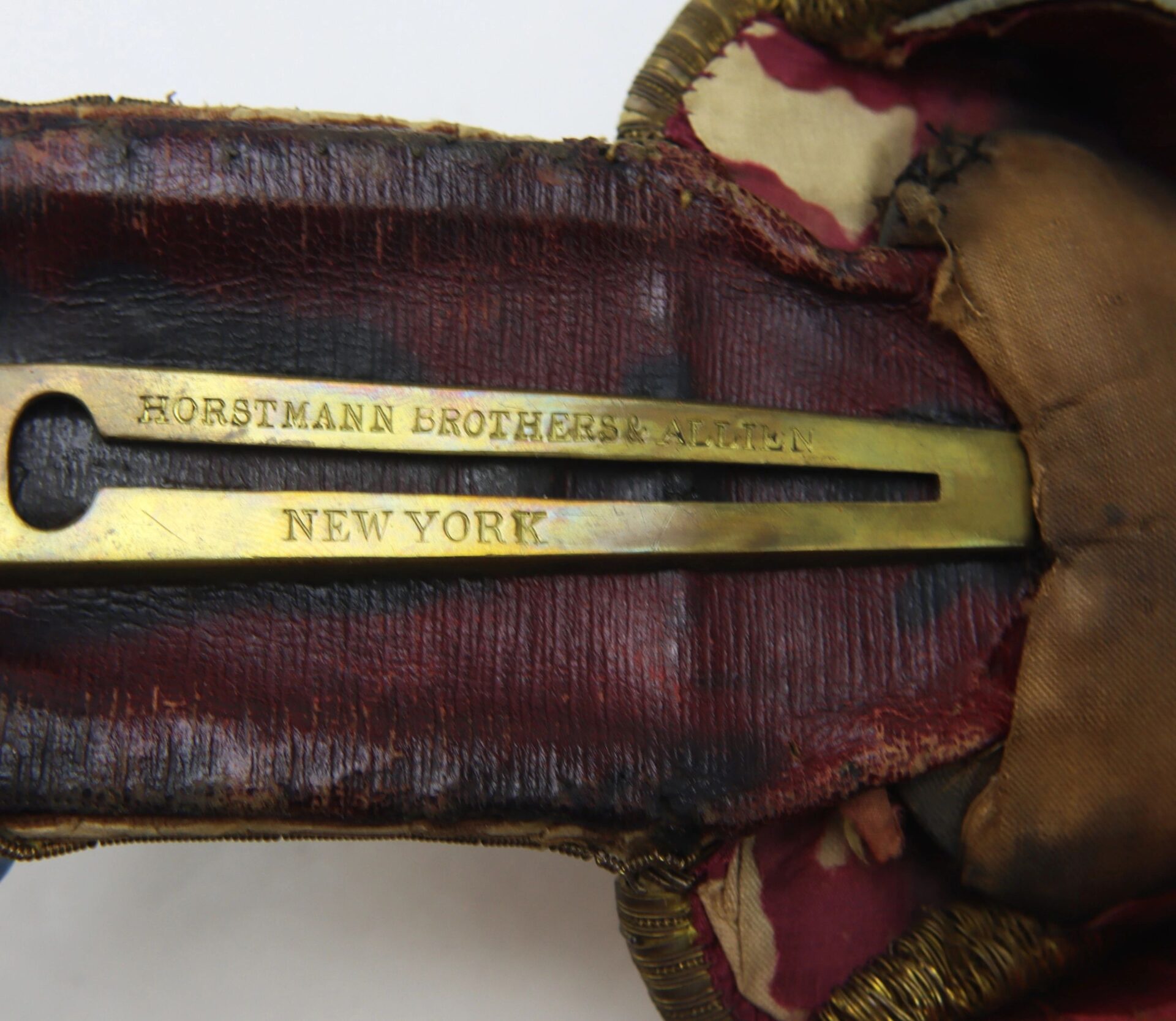 Close-up of a brass plate inside a worn, red-lined U.S. Officer’s Epaulettes, engraved with "HORSTMANN BROTHERS & ALLIEN NEW YORK.