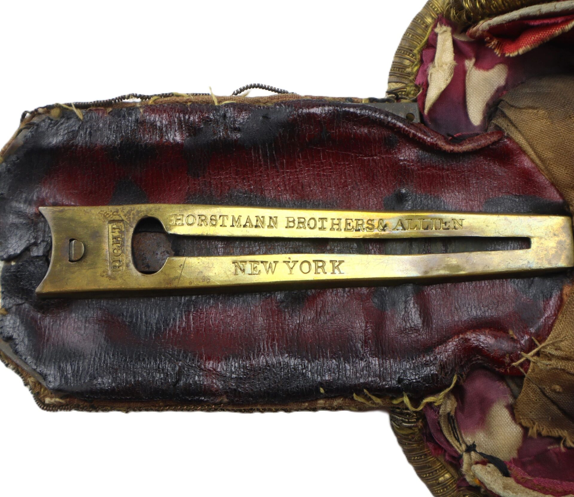 Close-up of a worn case for U.S. Officer’s Epaulettes with a brass label reading "HORSTMANN BROTHERS & ALLIEN NEW YORK" set against faded red and brown fabric.