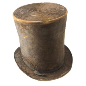 A worn, brown cylindrical "Top Hat Manufactured Ca. 1820" with a flat brim and thin, damaged ribbon, photographed against a white background.