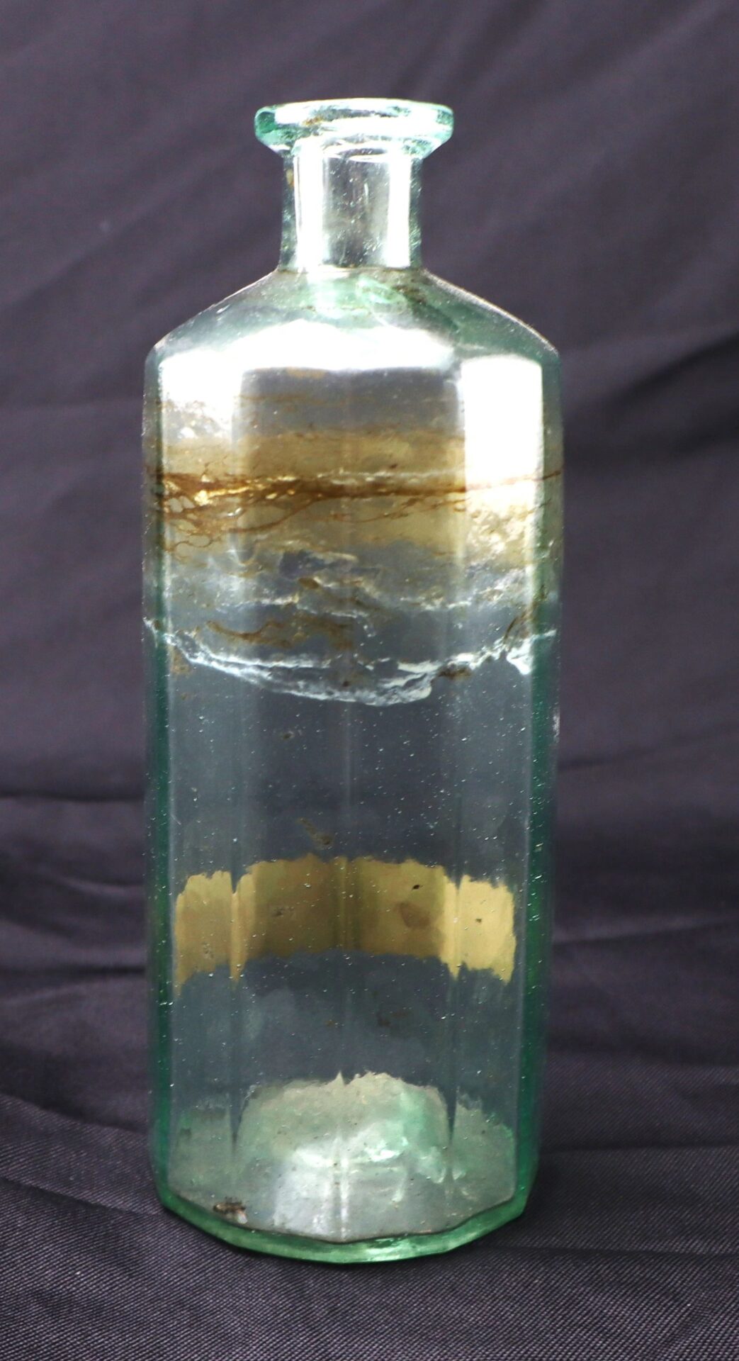 The Apothecary Bottle – Fluid Extract Hyssop is a vintage clear glass bottle with a narrow neck and visible residue inside, set against a dark background.