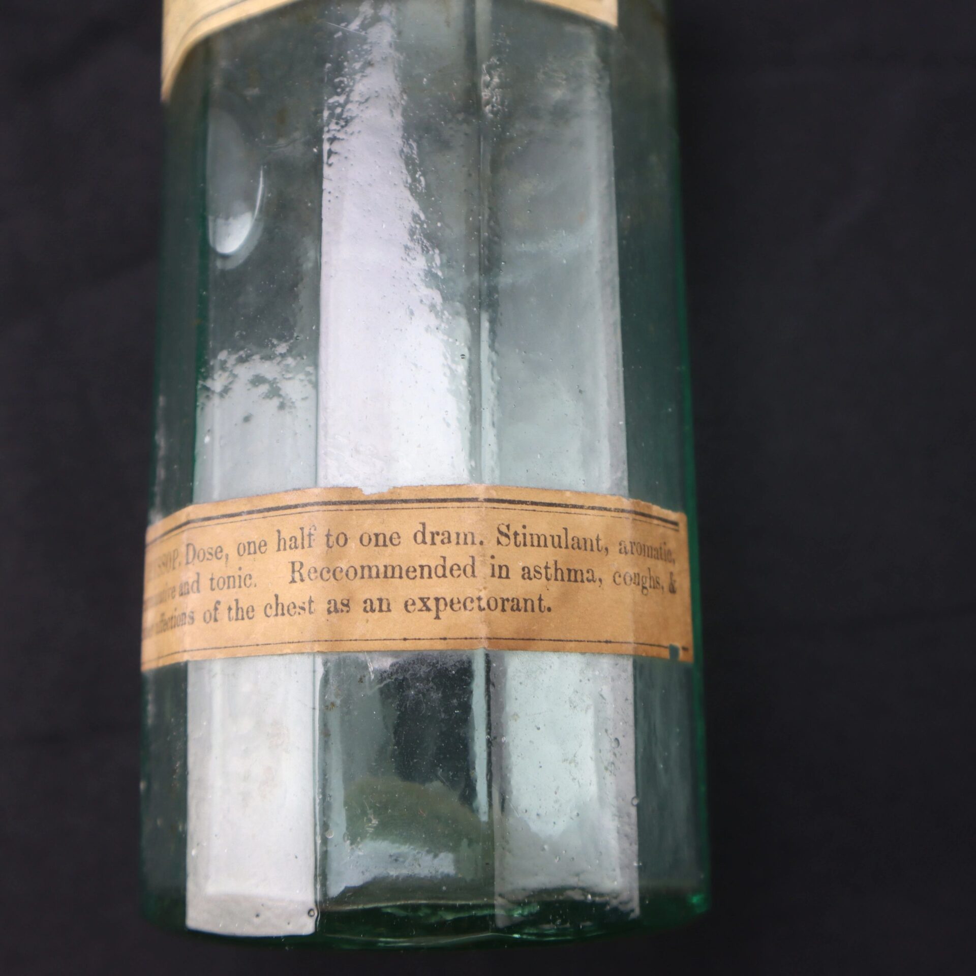 A vintage Apothecary Bottle – Fluid Extract Hyssop with a partially readable label recommending its use as an expectorant for asthma, coughs, and chest afflictions.