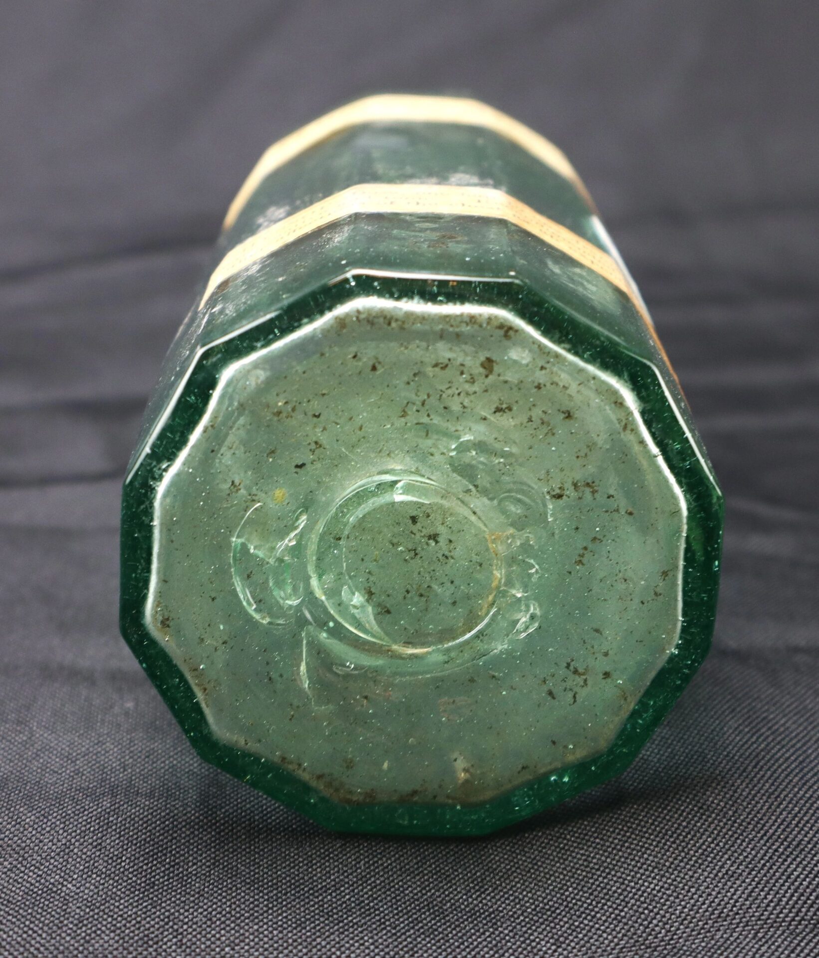 A close-up of the bottom of the green, octagonal Apothecary Bottle – Fluid Extract Hyssop rests on a dark fabric surface.