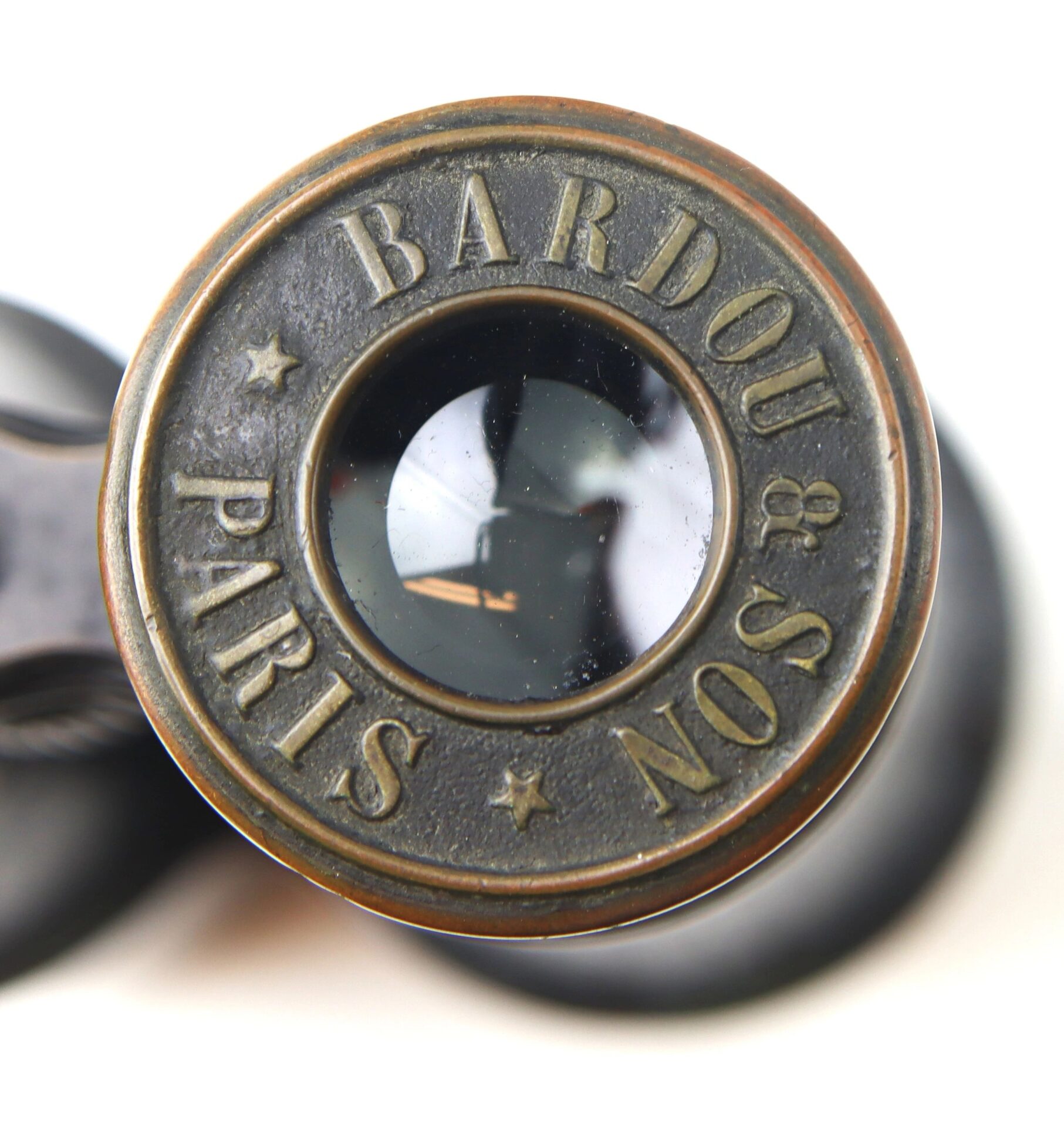 Close-up of a Bardou & Son Paris Binoculars lens, featuring the inscription "BARDOU PARIS No 83" around the glass element and visible reflections on the lens surface.
