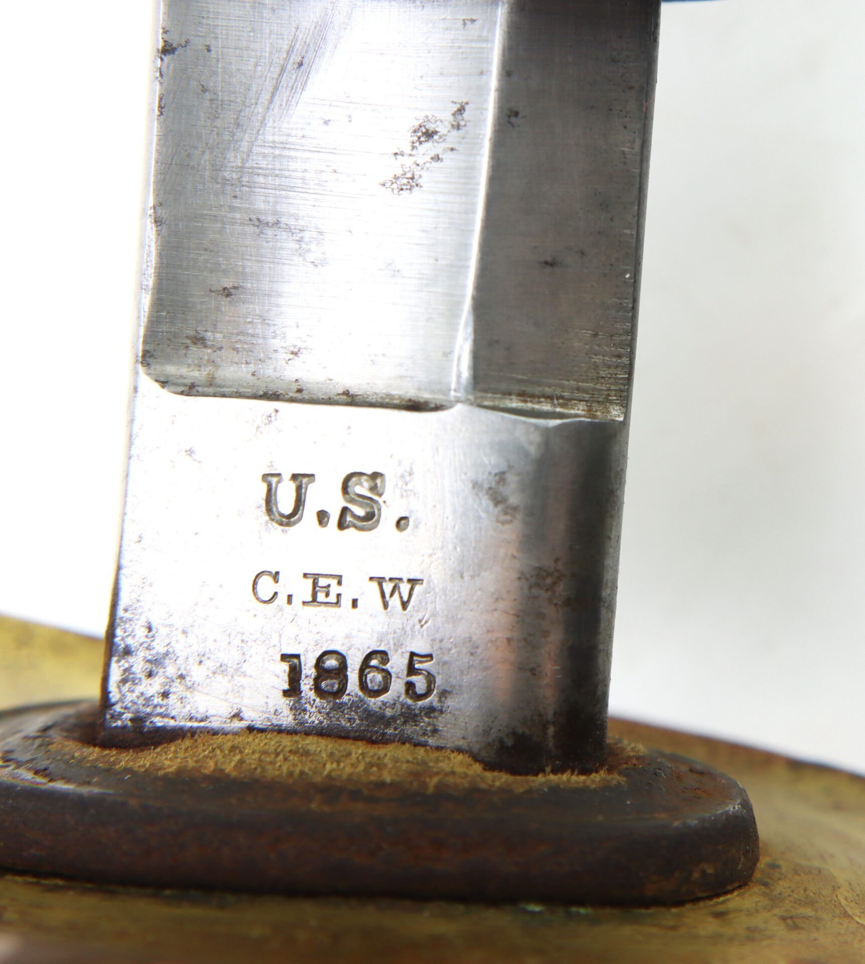 Close-up of a metal blade stamped with "U.S.", "C.E.W", and "1865" above a rusted metal guard.