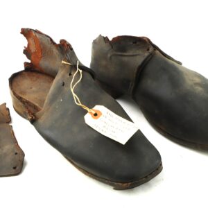 A pair of old, worn leather shoes with damaged heels and a handwritten tag attached, displayed on a white background.