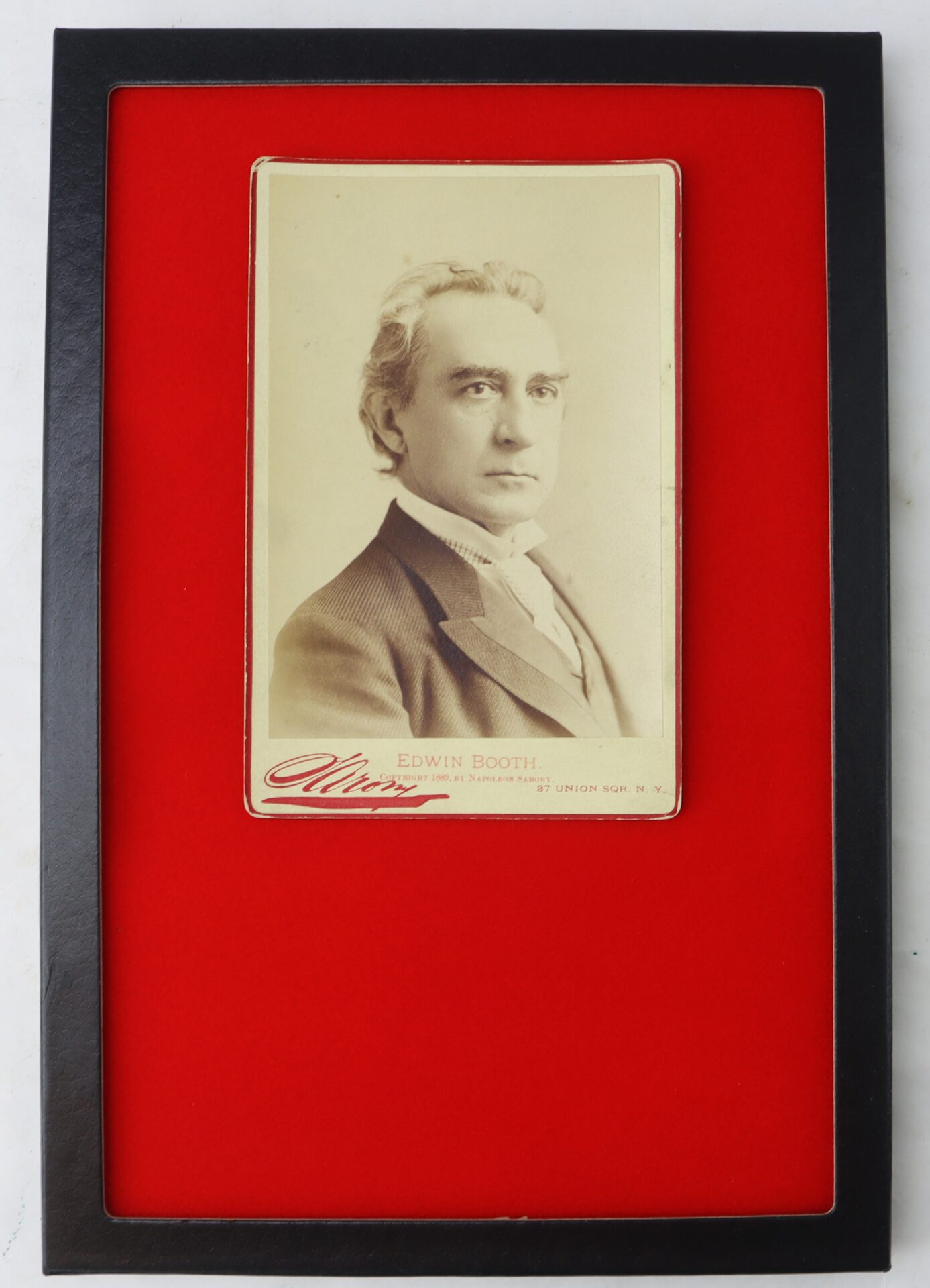 A sepia portrait photograph of a man in a suit, labeled "Edwin Booth," is displayed in a black frame with a red background.