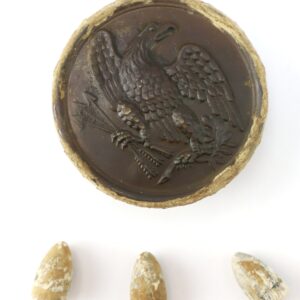 A round, worn military button with an eagle design above three aged, conical bullets on a white background.