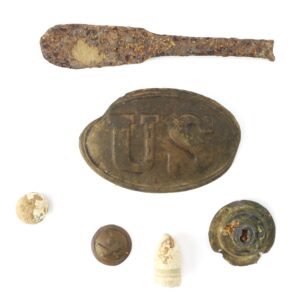 An assortment of old metal and lead relics, including a rusted knife, a brass U.S. belt plate, a bullet, buttons, and a circular corroded item, displayed on a white background.