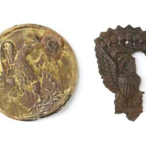 Two worn metal badges featuring eagle designs, displayed against a white background. The left badge is round and the right badge is irregularly shaped.