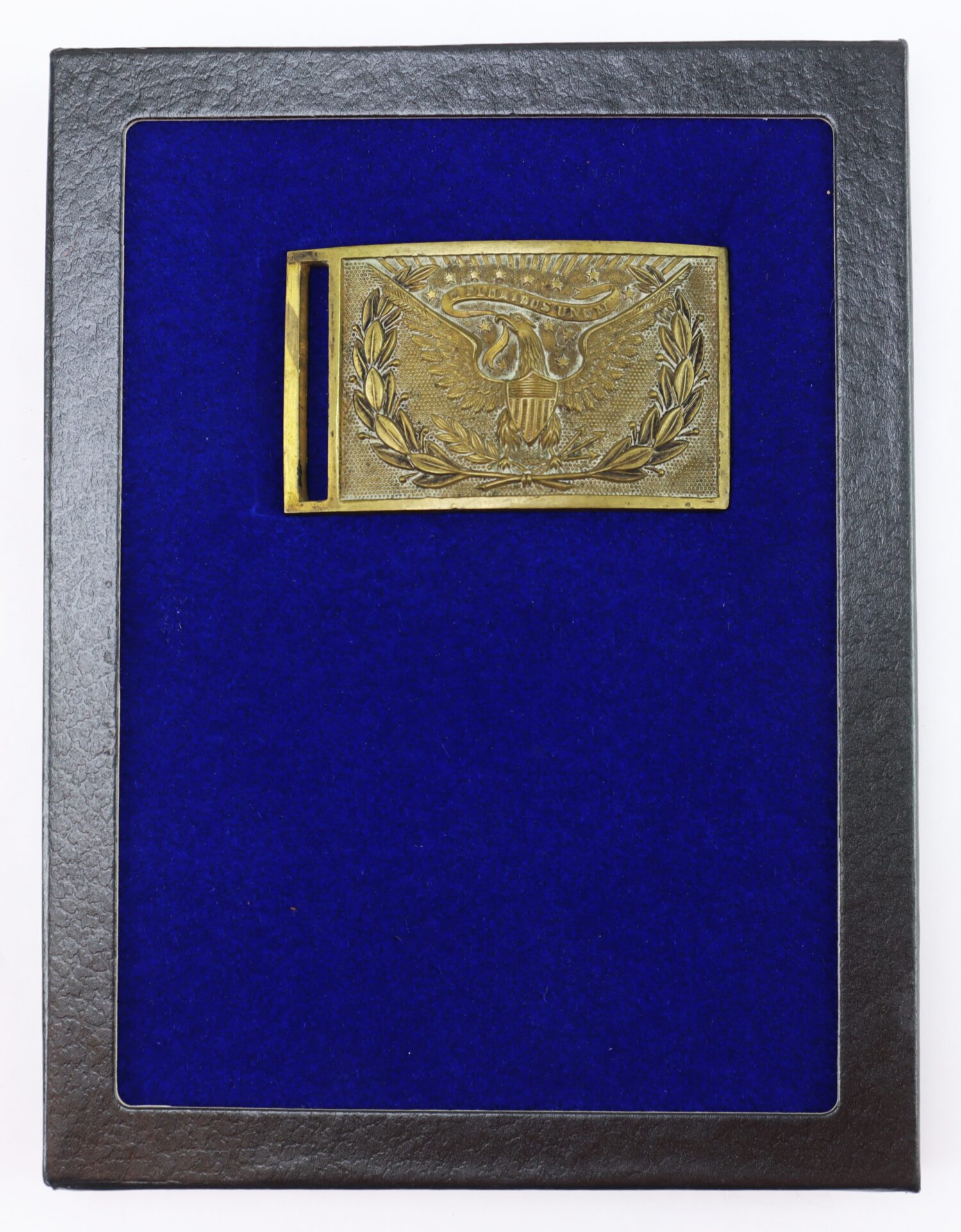 A rectangular brass belt buckle with an eagle and laurel design is displayed on a blue velvet background inside a black frame.