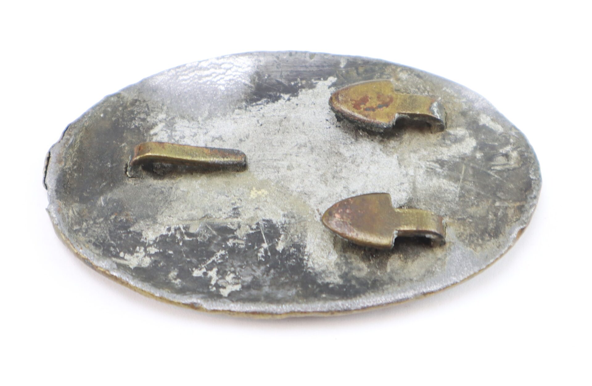 The Civil War U.S. Cartridge Box Plate is an oval-shaped metal item with a rough surface and two bent metal prongs on the back, displayed against a white background.