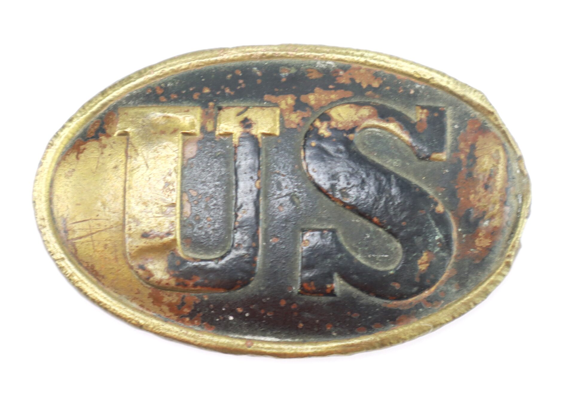 An oval, weathered brass and black Civil War U.S. Cartridge Box Plate featuring raised "US" letters on its surface.