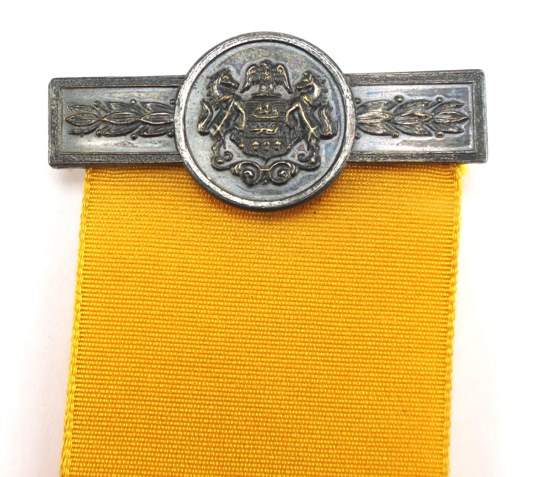 A silver metal badge with a crest and laurel design is attached to a wide yellow ribbon.