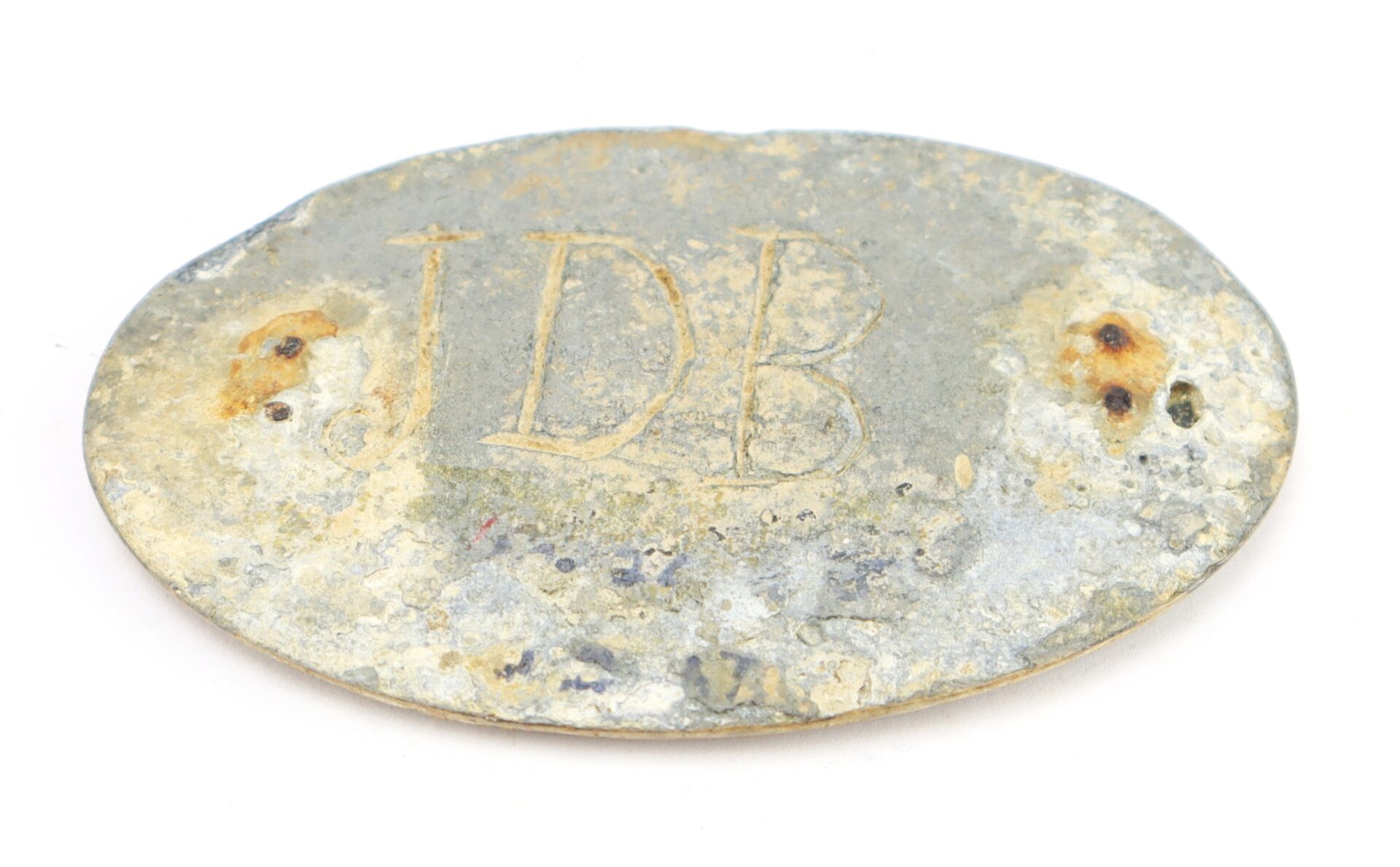 Oval-shaped, weathered metal tag with the engraved initials "JDB" and two discolored holes on either side.